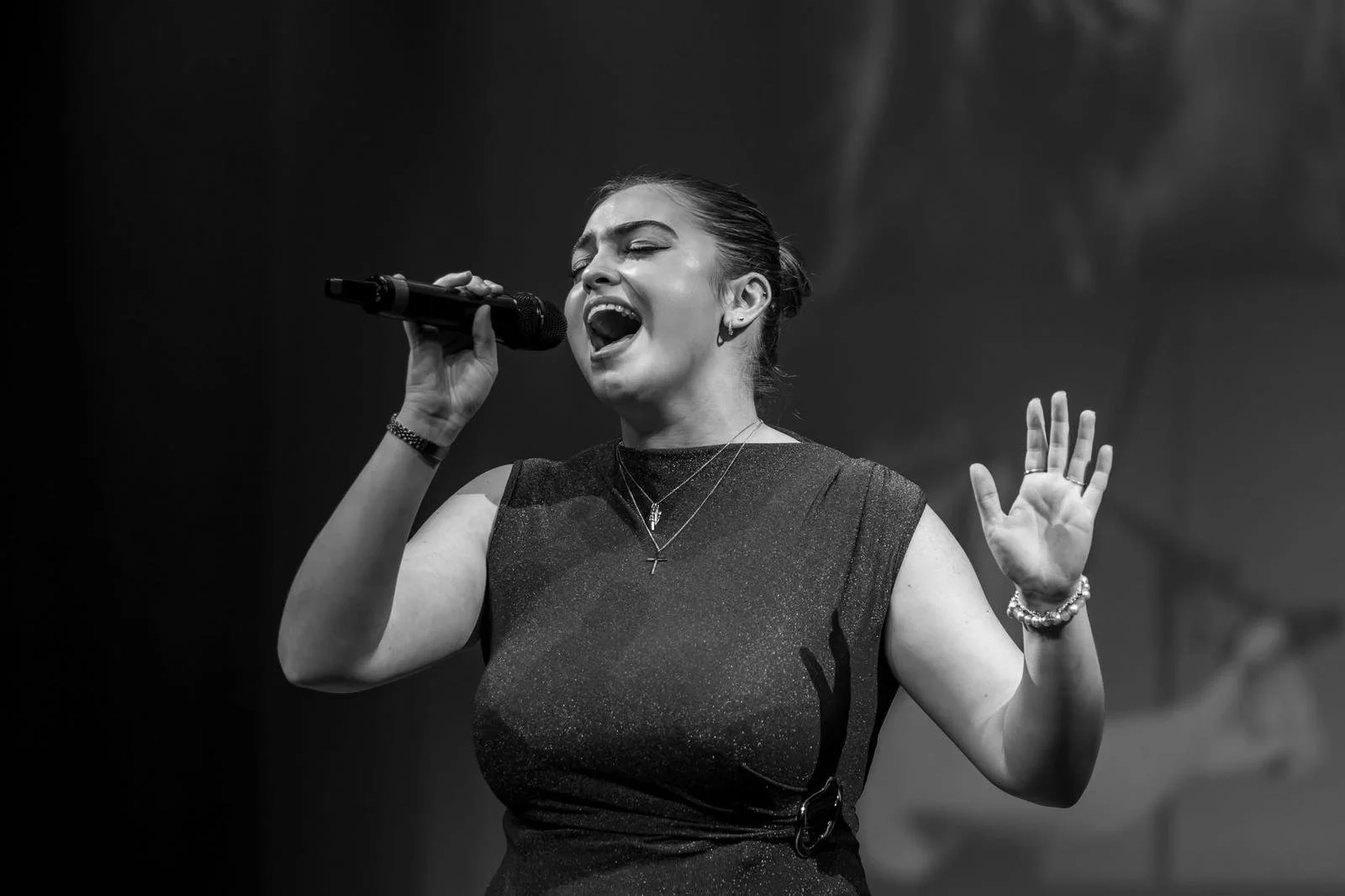 A woman singing into a microphone on stage, with her eyes closed and one hand raised, in black and white.
