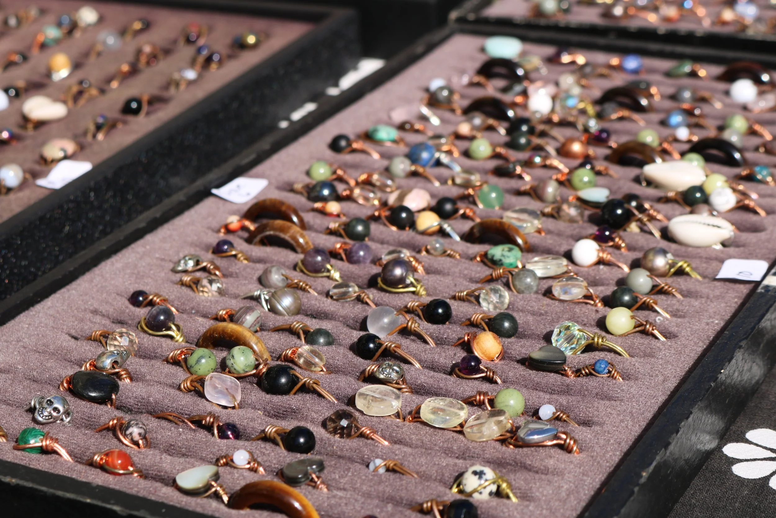 A display of various rings with stones and beads arranged on a brown fabric surface.