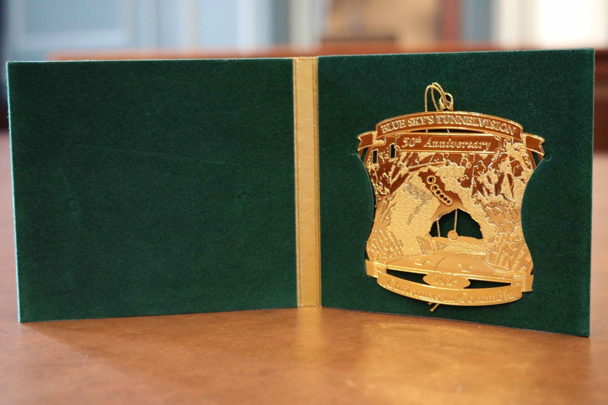 Gold medal ornament design, commemorating the 50th anniversary of Blue Skies Tunnel Vision, displayed on a green presentation folder.