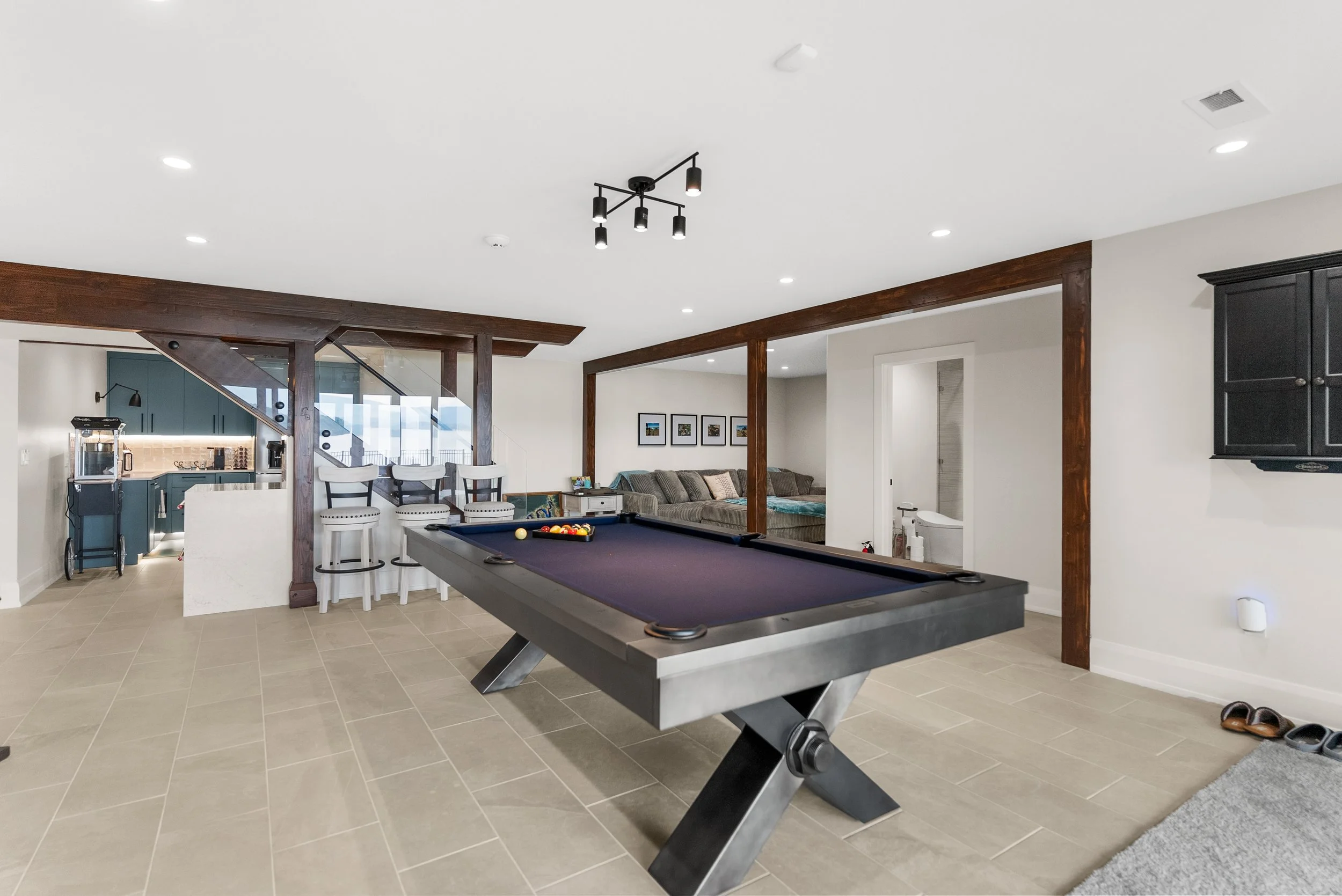Living area with a pool table, a gray couch, a bar with four chairs, and framed pictures on the wall.