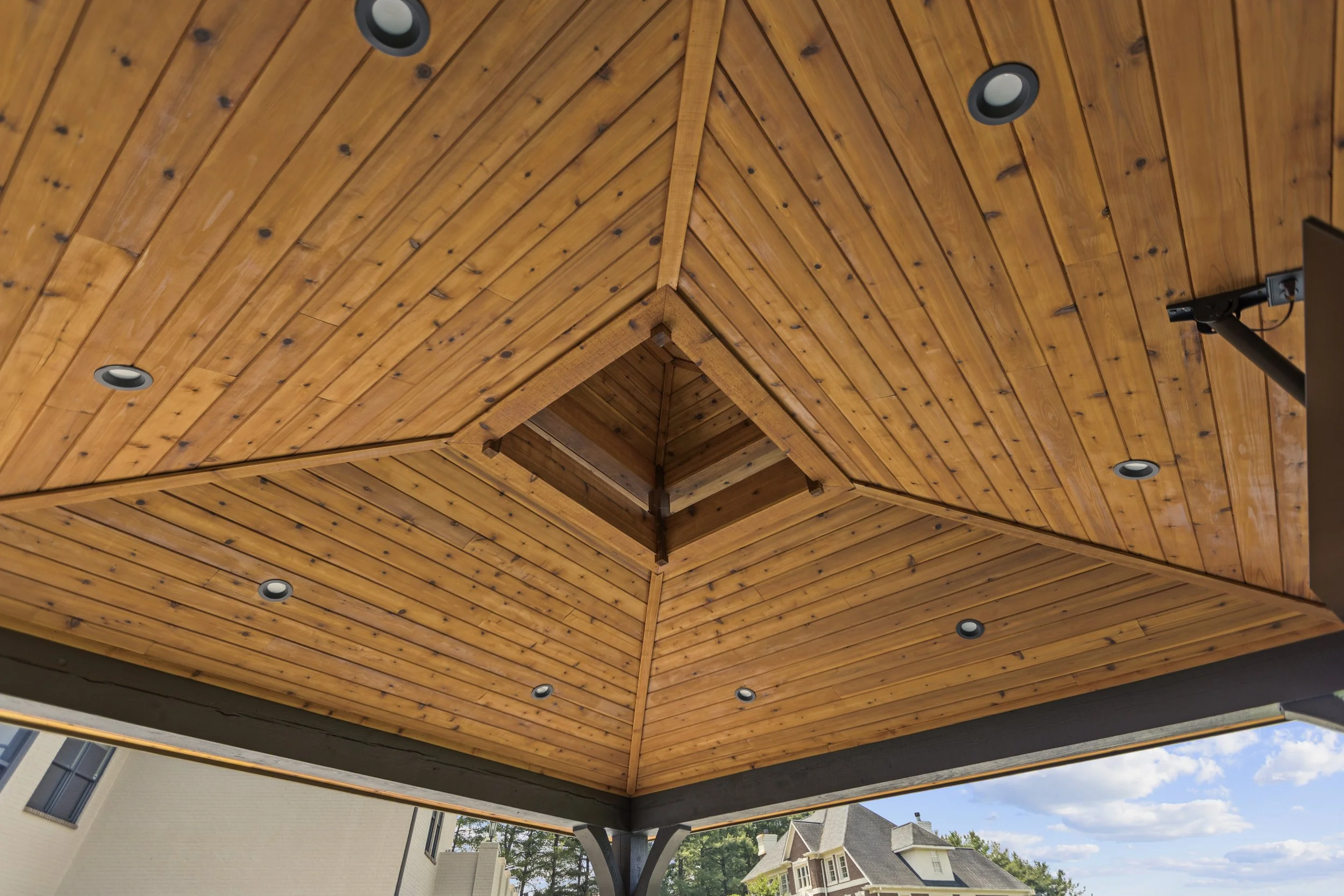 A wooden ceiling with recessed lighting and a metal support structure outside of modern houses.