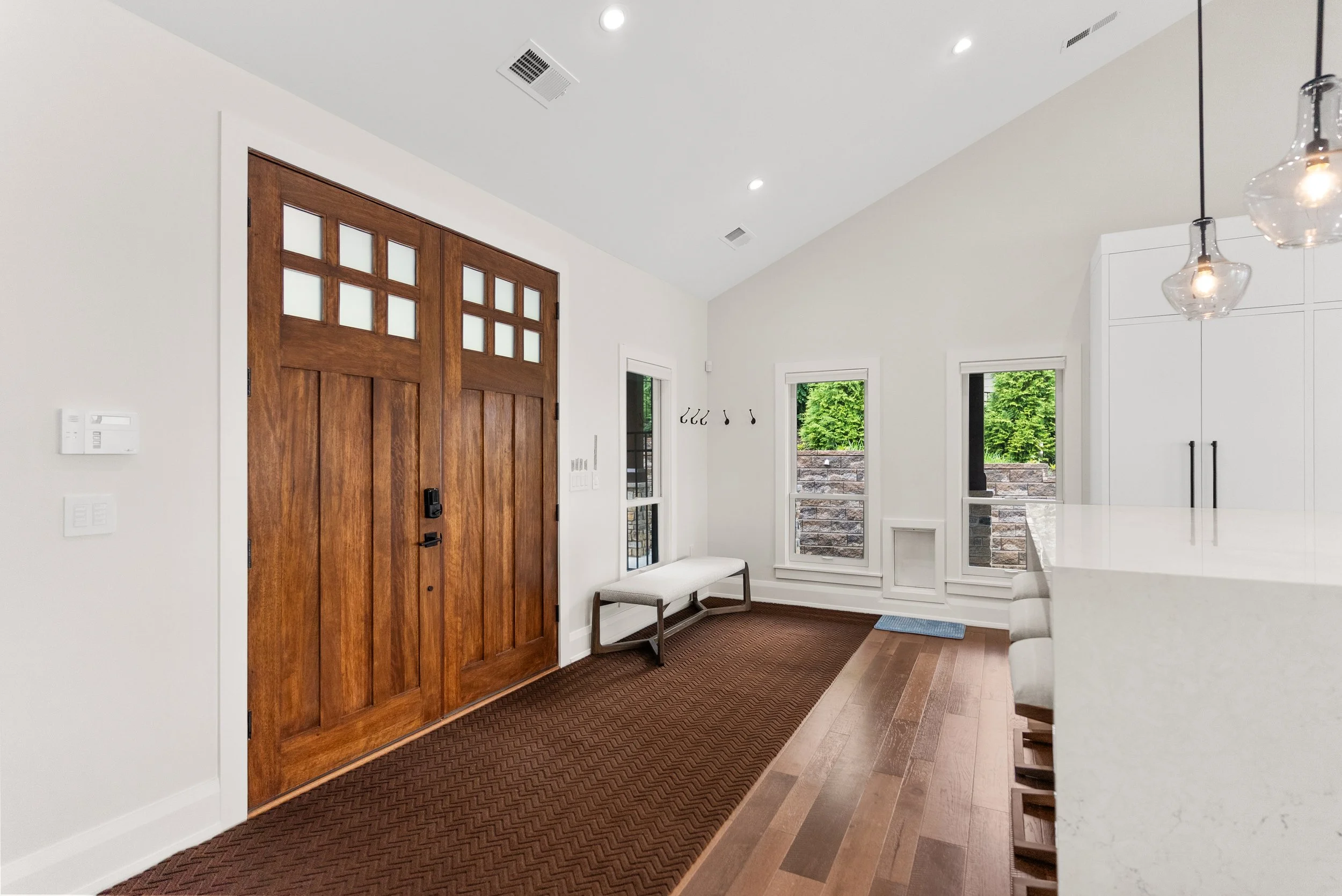 Modern entryway with wooden front door, white walls, large windows, and a bench near the door.