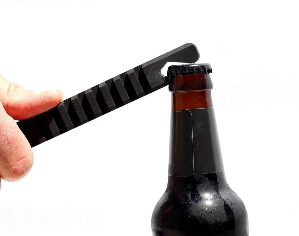 Black anodized aluminum tactical bottle opener prying the cap off a beer bottle