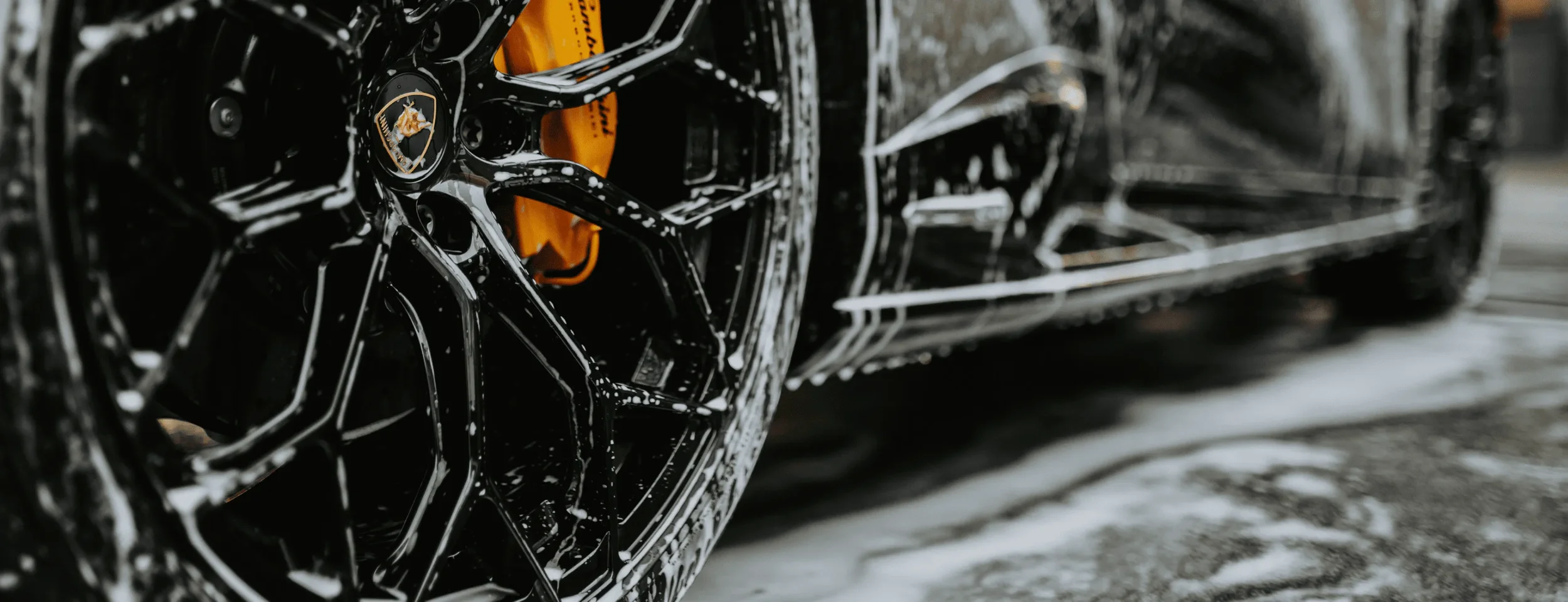 Close-up of a black luxury car's wheel and tire, with water droplets on the surface.