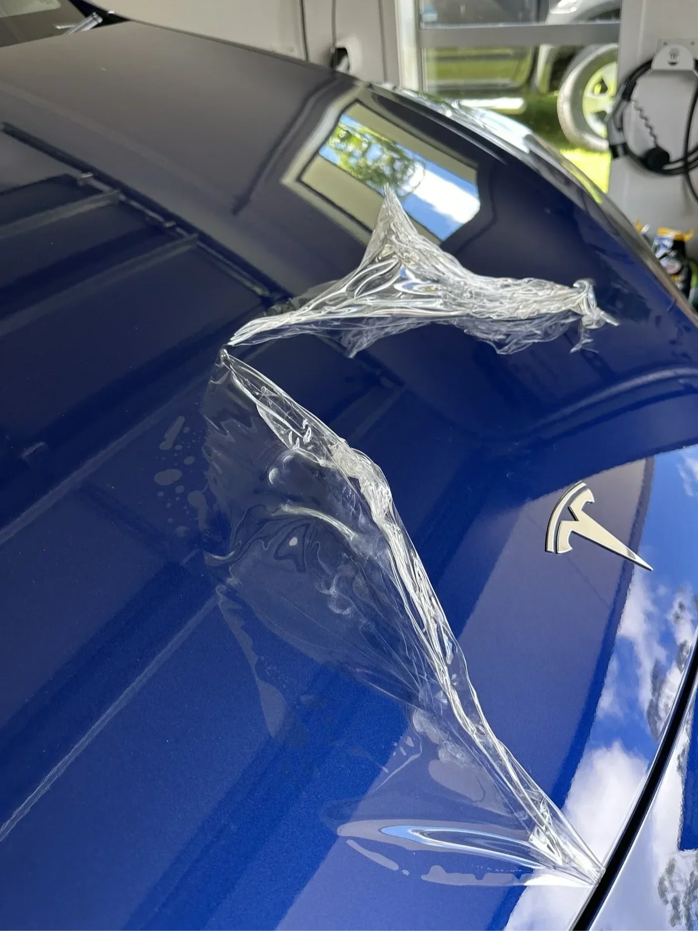 Close-up of a blue car with a crack and peeling paint on the hood near the windshield, in a garage or workshop setting.
