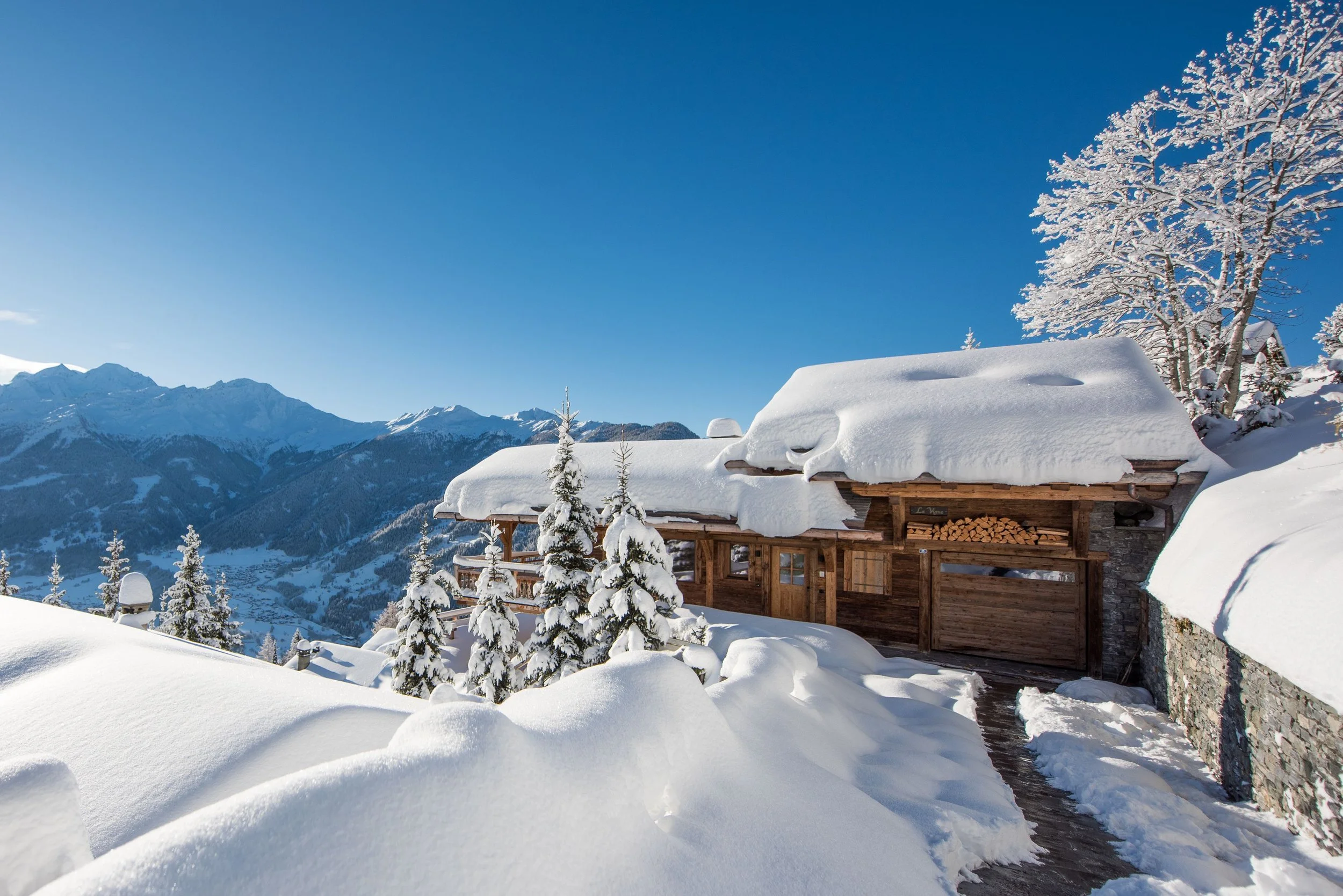 Chalet la Vigne exterior in deep snow on a bluebird day with Alpine mountain views, Verbier Switzerland