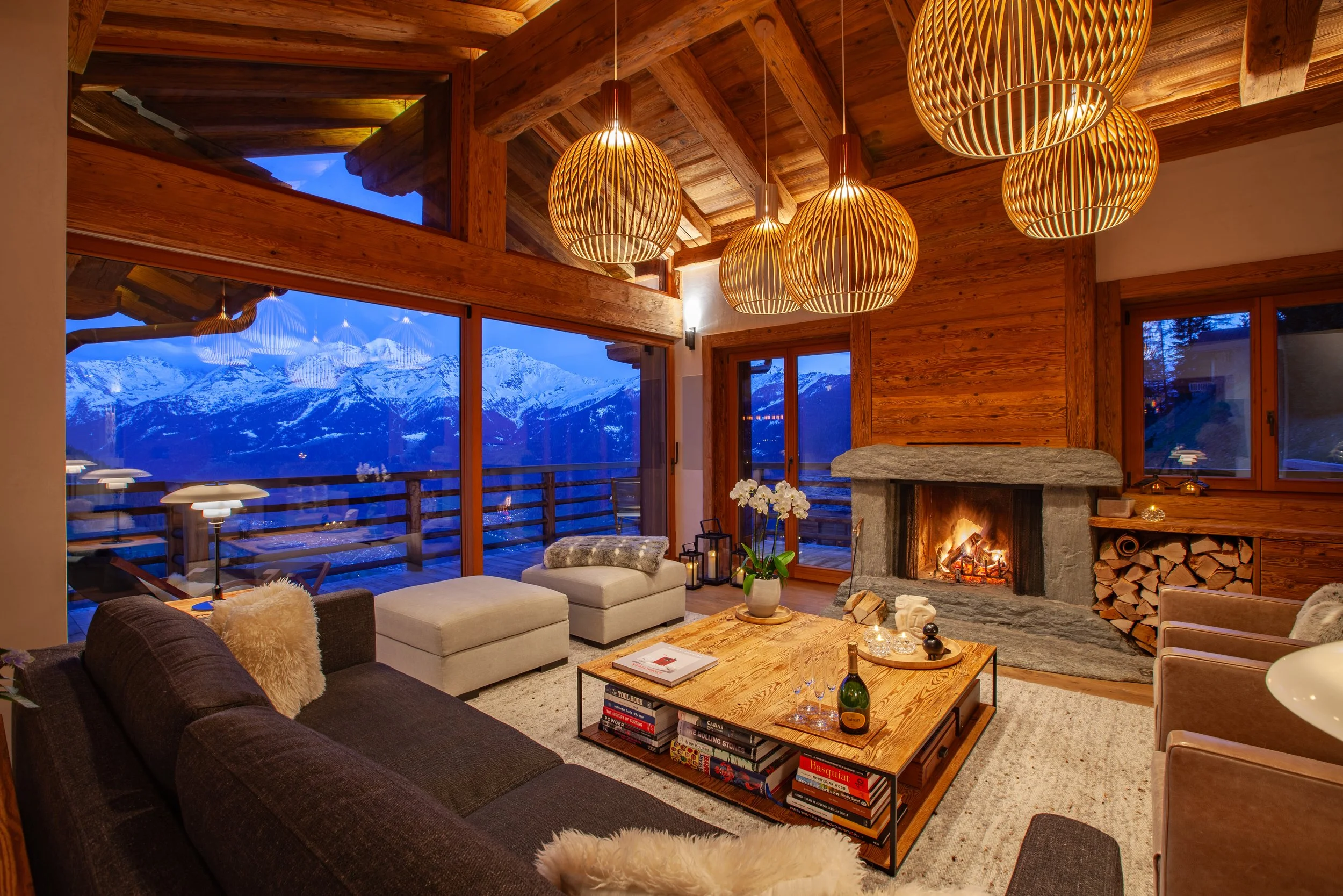 Living room at dusk with Ruinart champagne, roaring fire and panoramic Alpine mountain views, Chalet la Vigne Verbier Switzerland