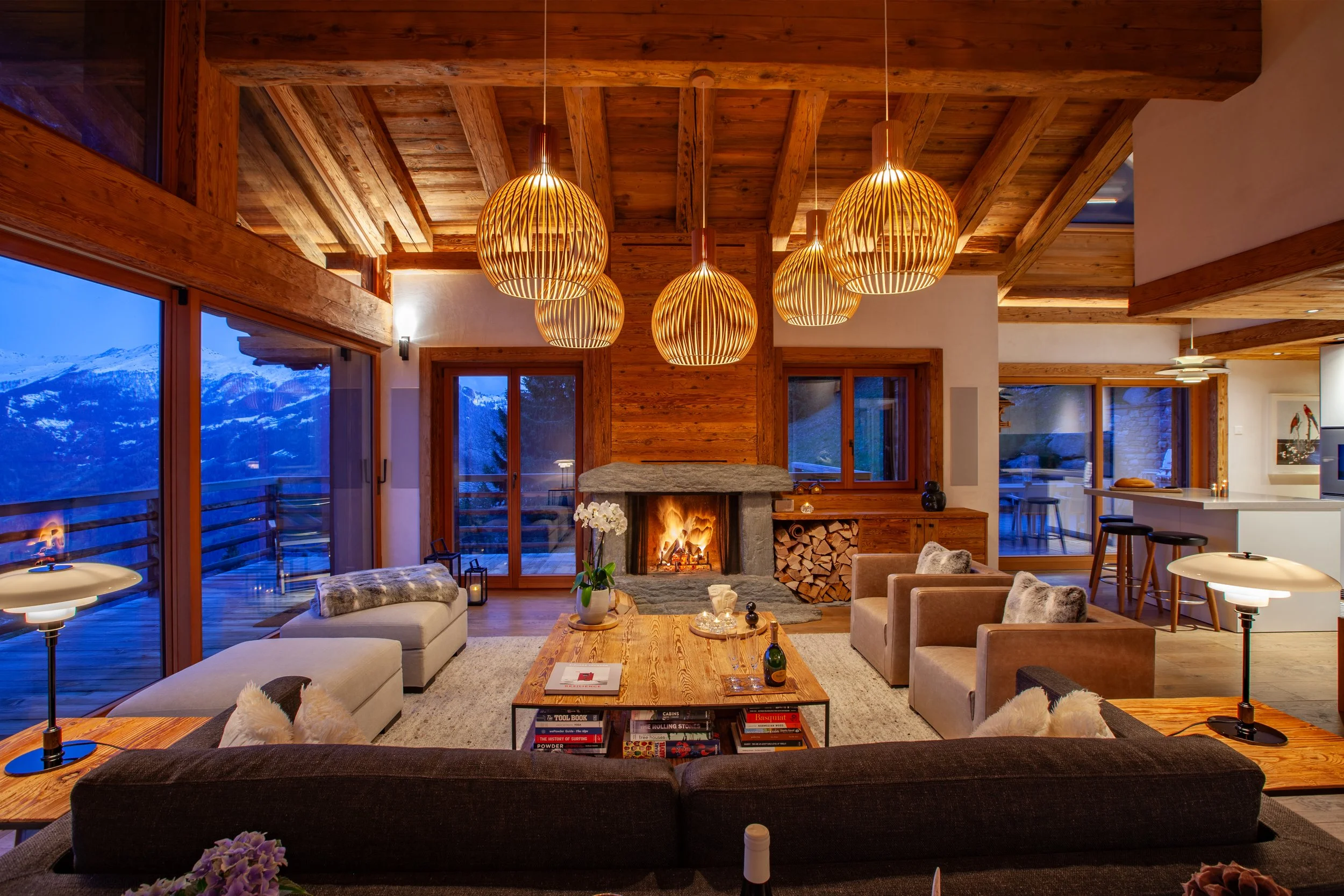 Living room at dusk with roaring fire, Meridiani furniture, Louis Poulsen lighting and Ruinart champagne, Chalet la Vigne Verbier Switzerland
