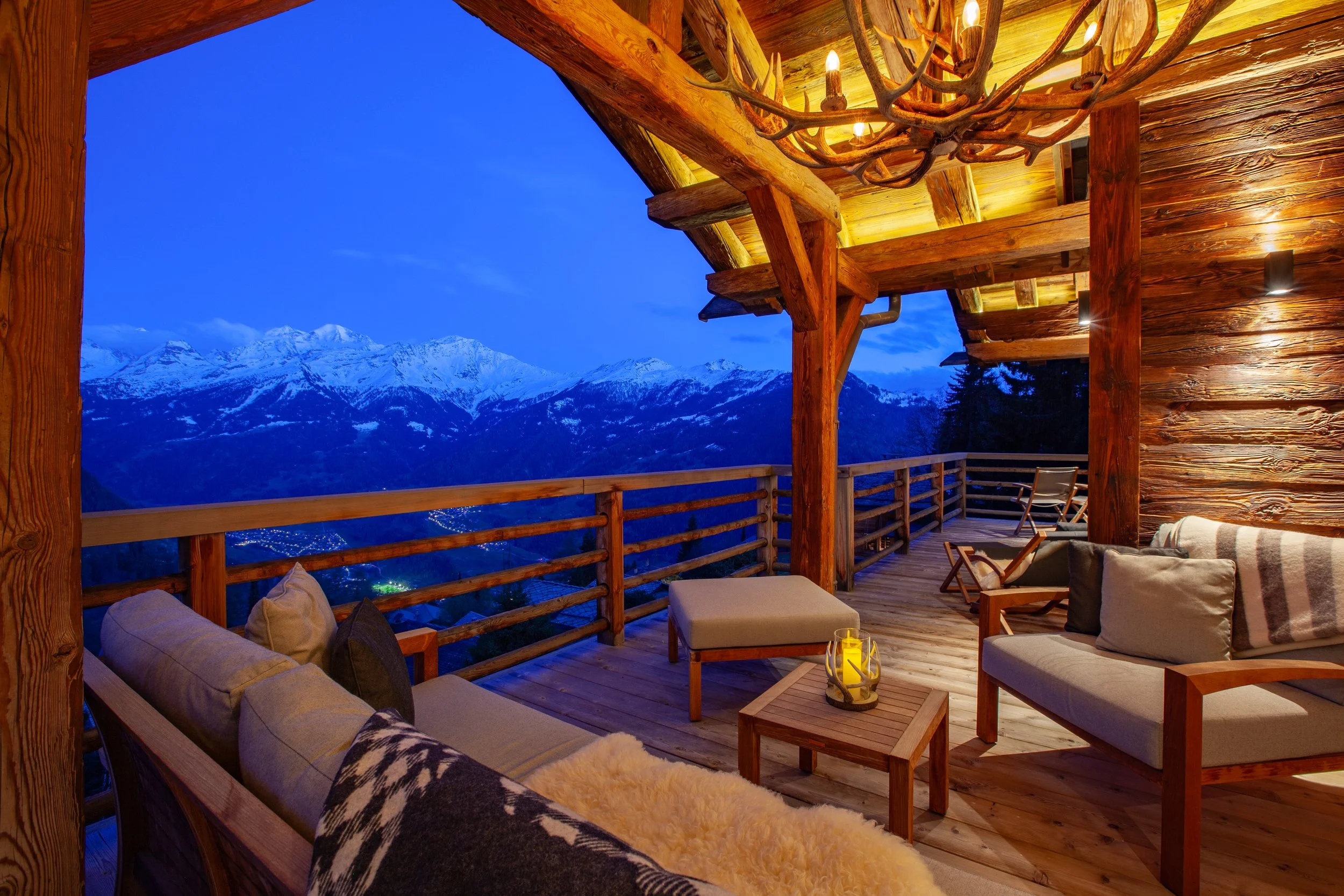 Covered terrace at dusk with Big Mountain Antlers chandelier, Royal Botania furniture and fur throws, panoramic Alpine views, Chalet la Vigne Verbier Switzerland