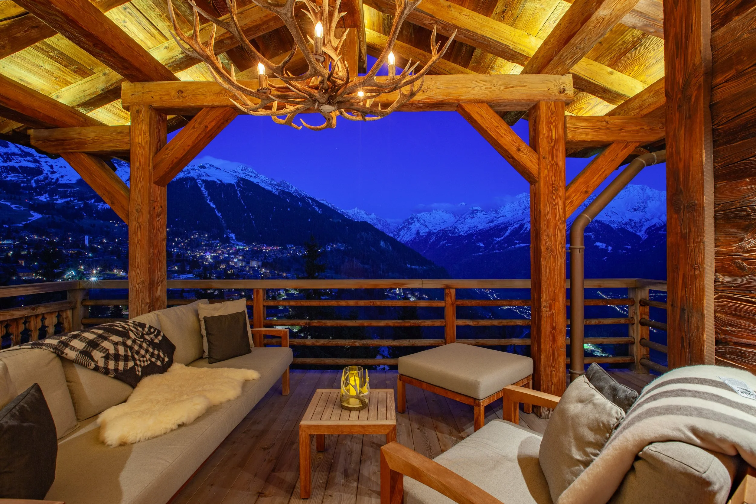 Covered terrace at dusk with Royal Botania teak furniture, Big Mountain Antlers chandelier and panoramic Alpine views, Chalet la Vigne Verbier Switzerland