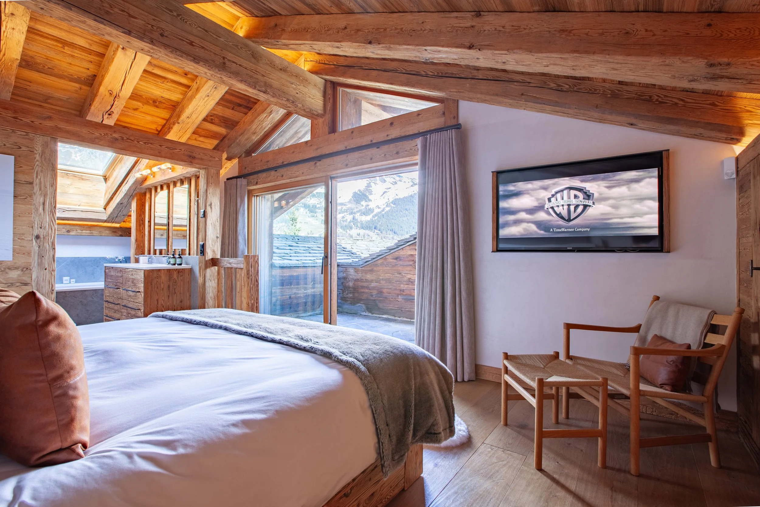Master bedroom suite with views of Verbier's Attelas couloirs, wall mounted TV, Carl Hansen chair and ottoman, Chalet la Vigne Switzerland