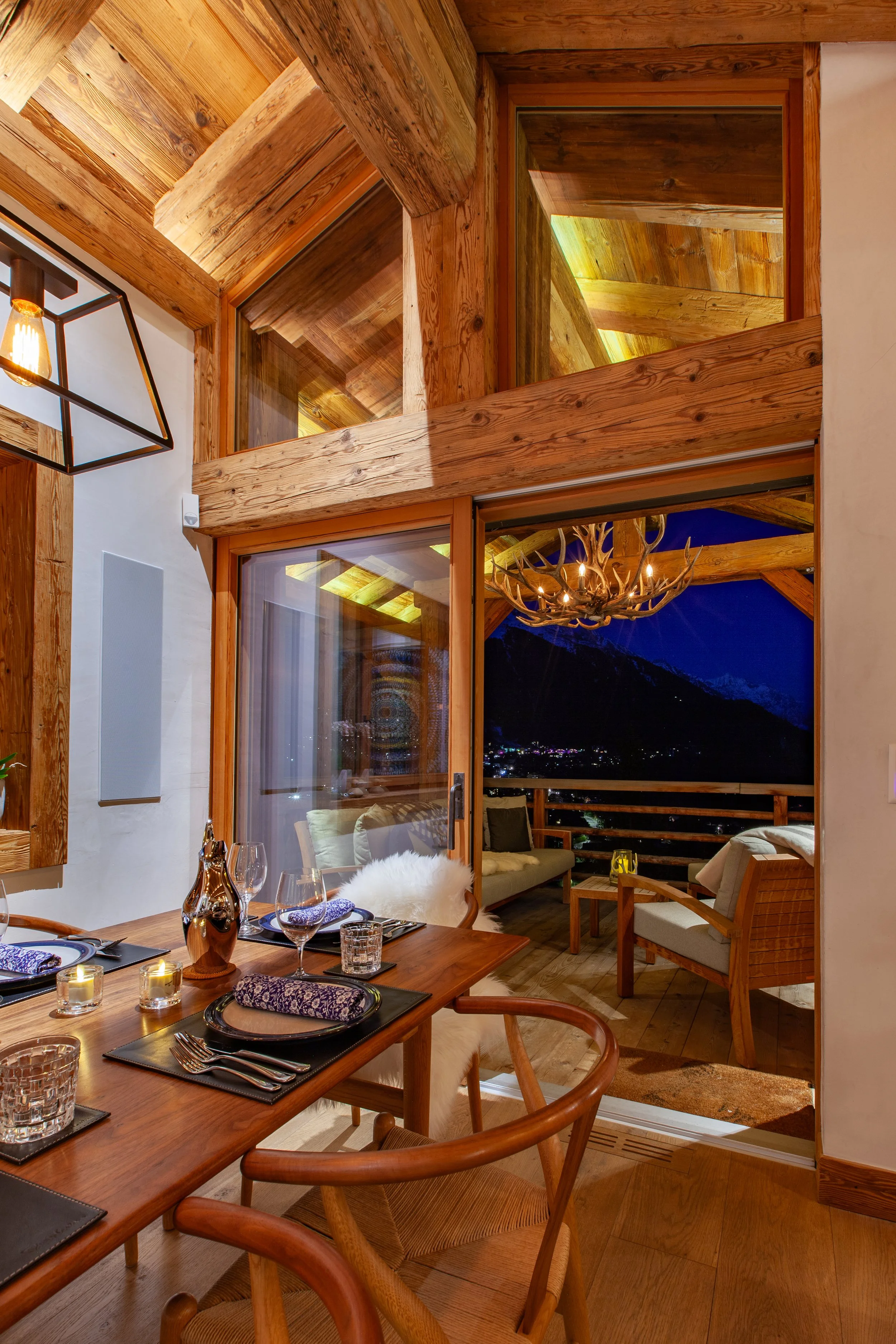 Dining room with open doors to covered terrace and lights of Verbier in the distance, Chalet la Vigne Switzerland