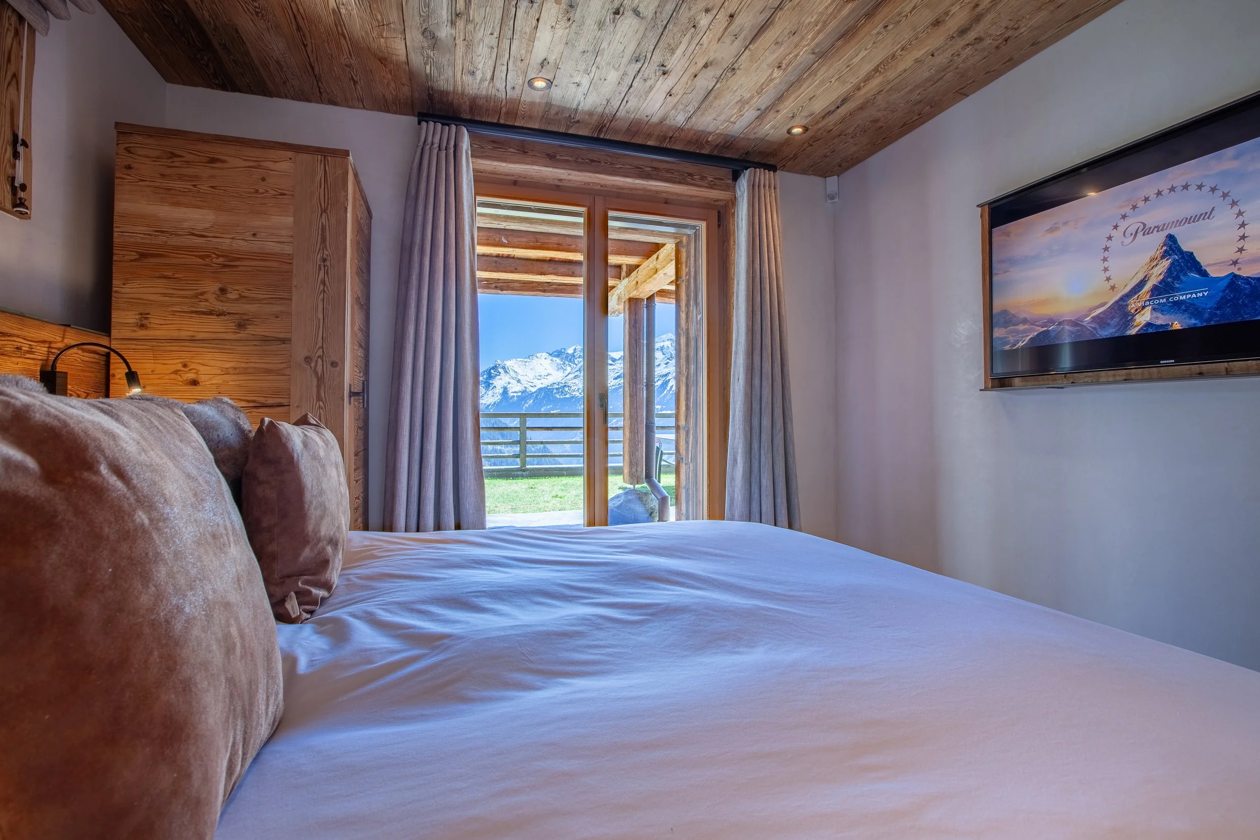 Bedroom with king size bed, wall mounted TV and stunning Alpine views through floor to ceiling windows, Chalet la Vigne Verbier
