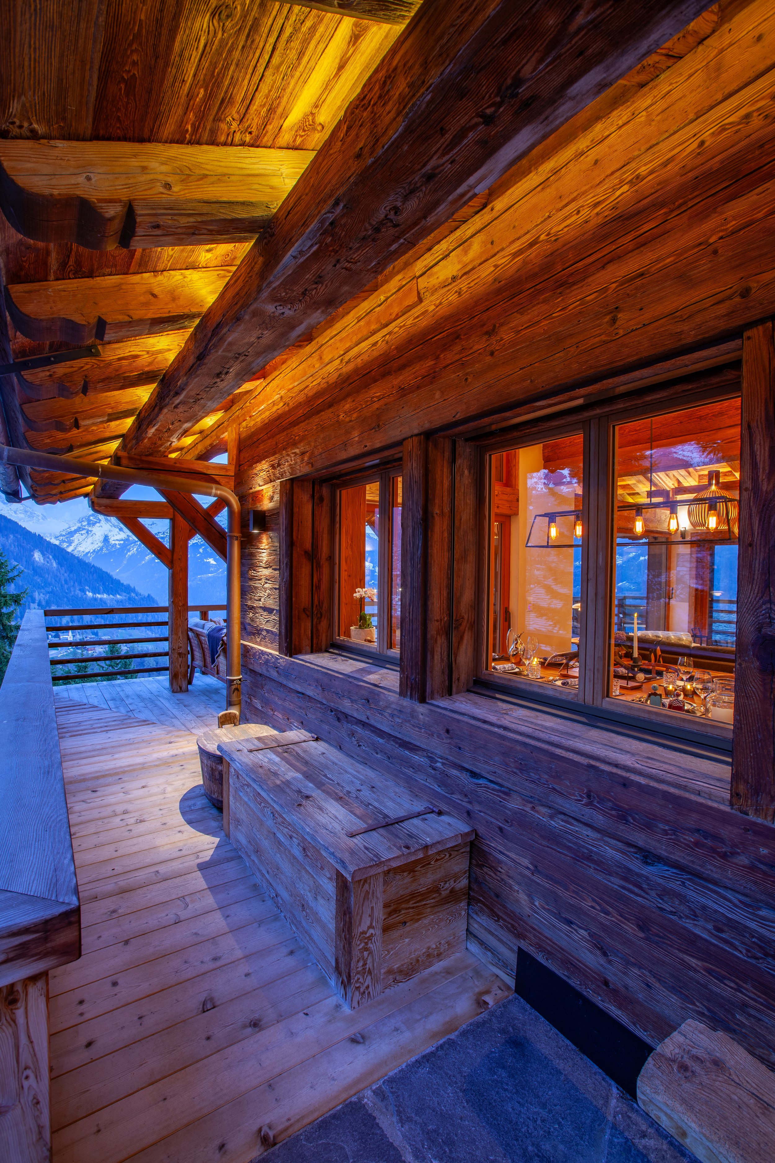 Chalet la Vigne exterior at dusk showing covered terrace and dining room with set table, Verbier Switzerland