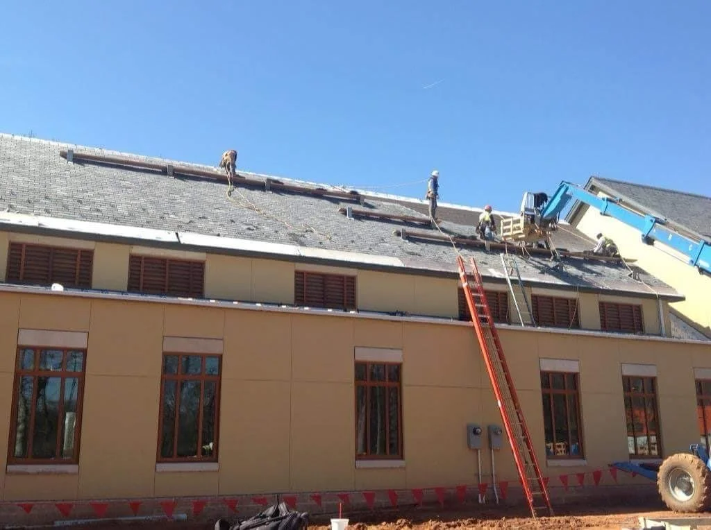 Construction workers on a roof of a building with safety ropes, a ladder, and a crane.