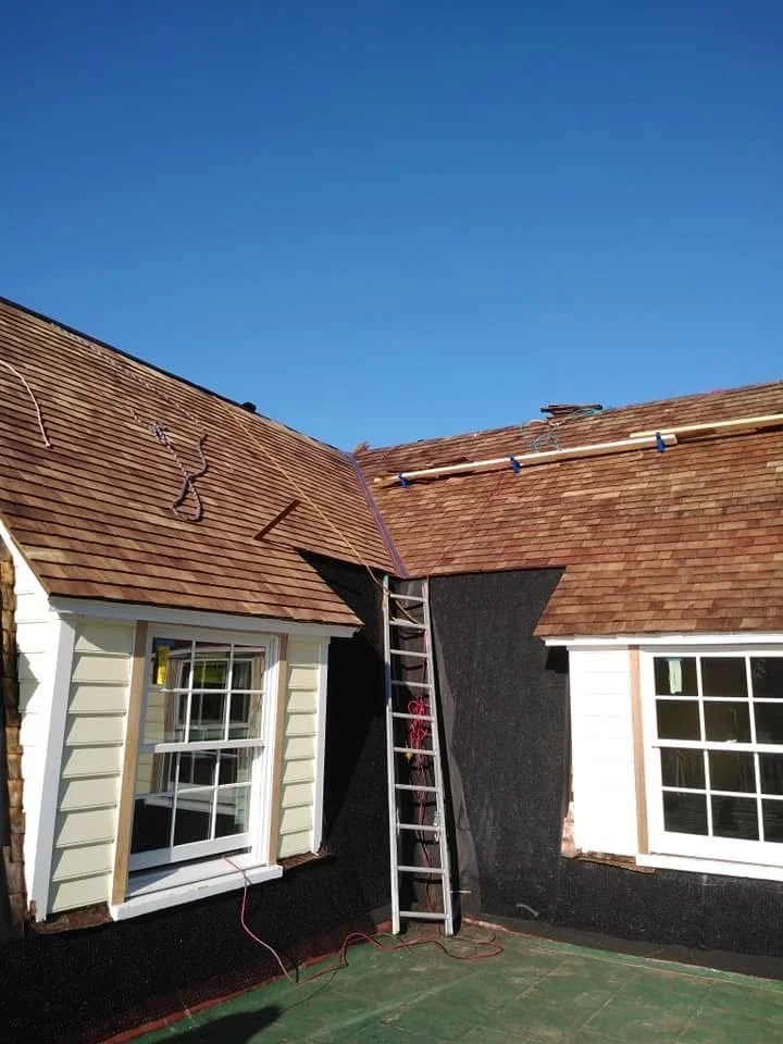 Ladder leaning against a house under renovation, with roofing work in progress on the roof, in a clear blue sky.
