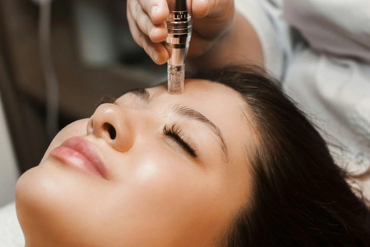 A woman receiving a facial treatment with a small device held above her forehead by a practitioner.
