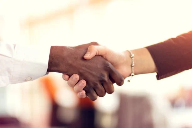 Close-up of two people shaking hands, one with dark skin and the other with light skin, in a professional setting.