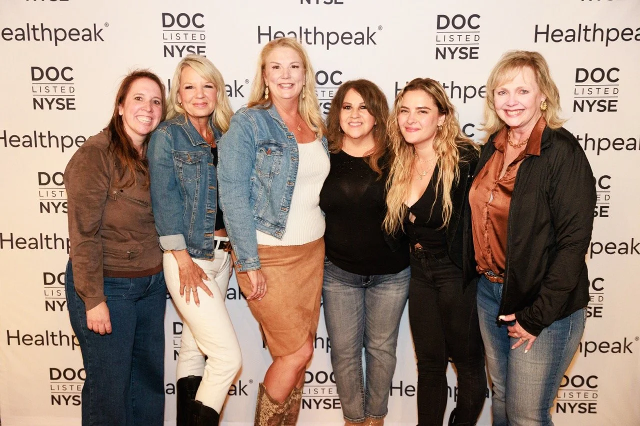 Six women standing together in front of a backdrop with logos for Healthpeak, DOC Listed NYSE, and NYSE, smiling for a photo at an event.