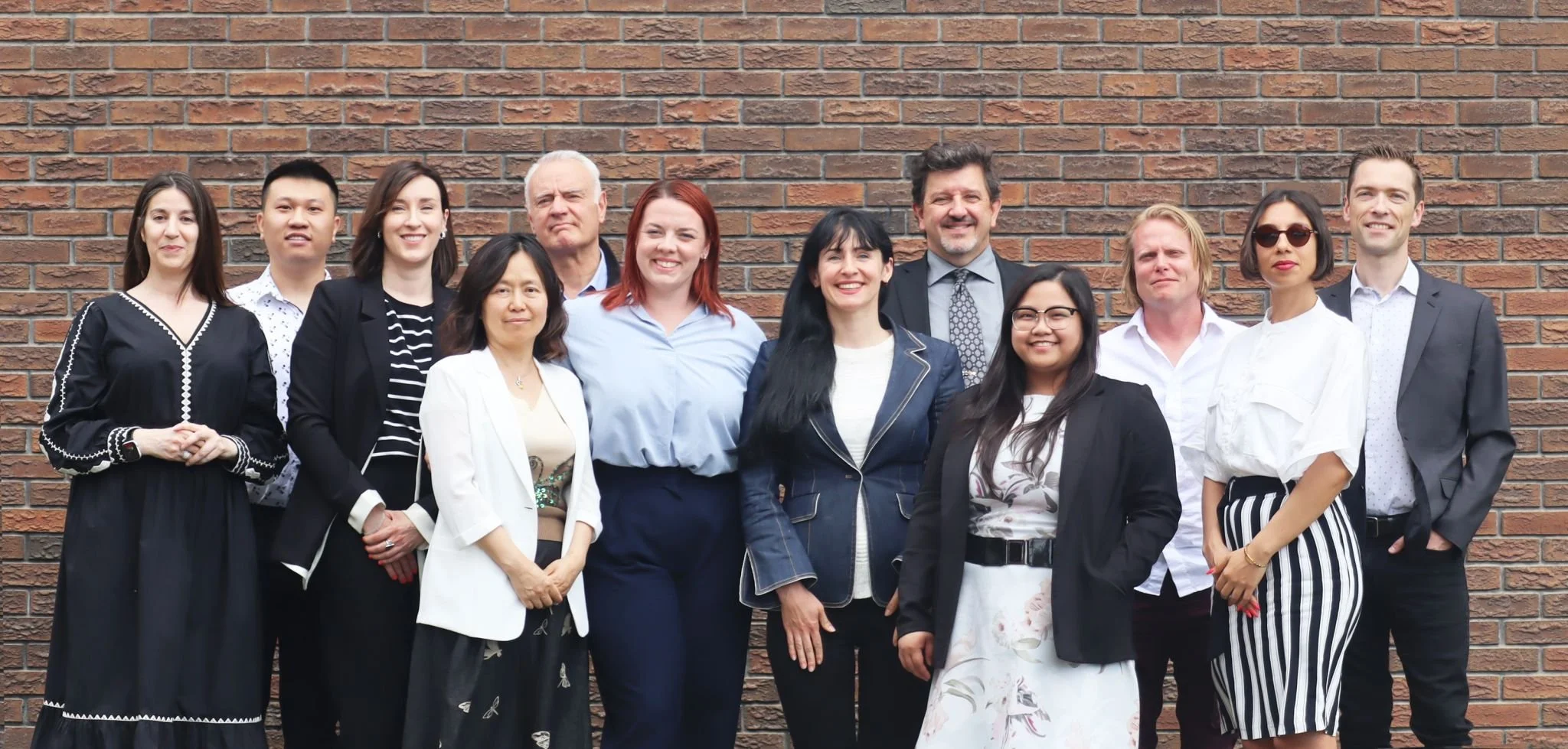 Group of diverse professionals standing in front of a brick wall, smiling.