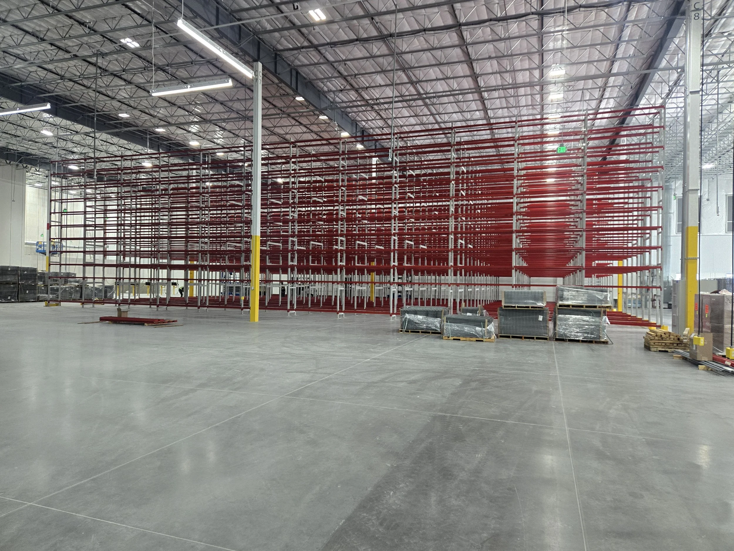 Interior of a large warehouse with a high ceiling, metal shelves, and palletized boxes and equipment.