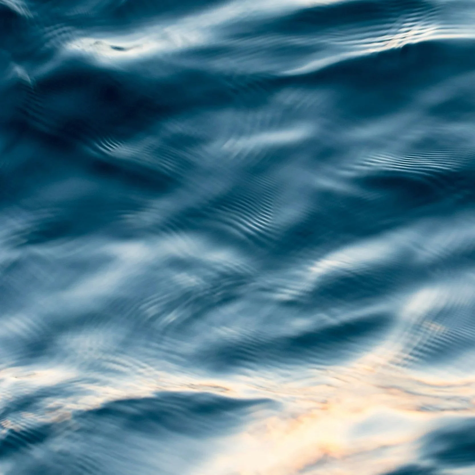 Close-up view of rippling water with a mix of blue hues and a hint of sunset colors near the bottom.