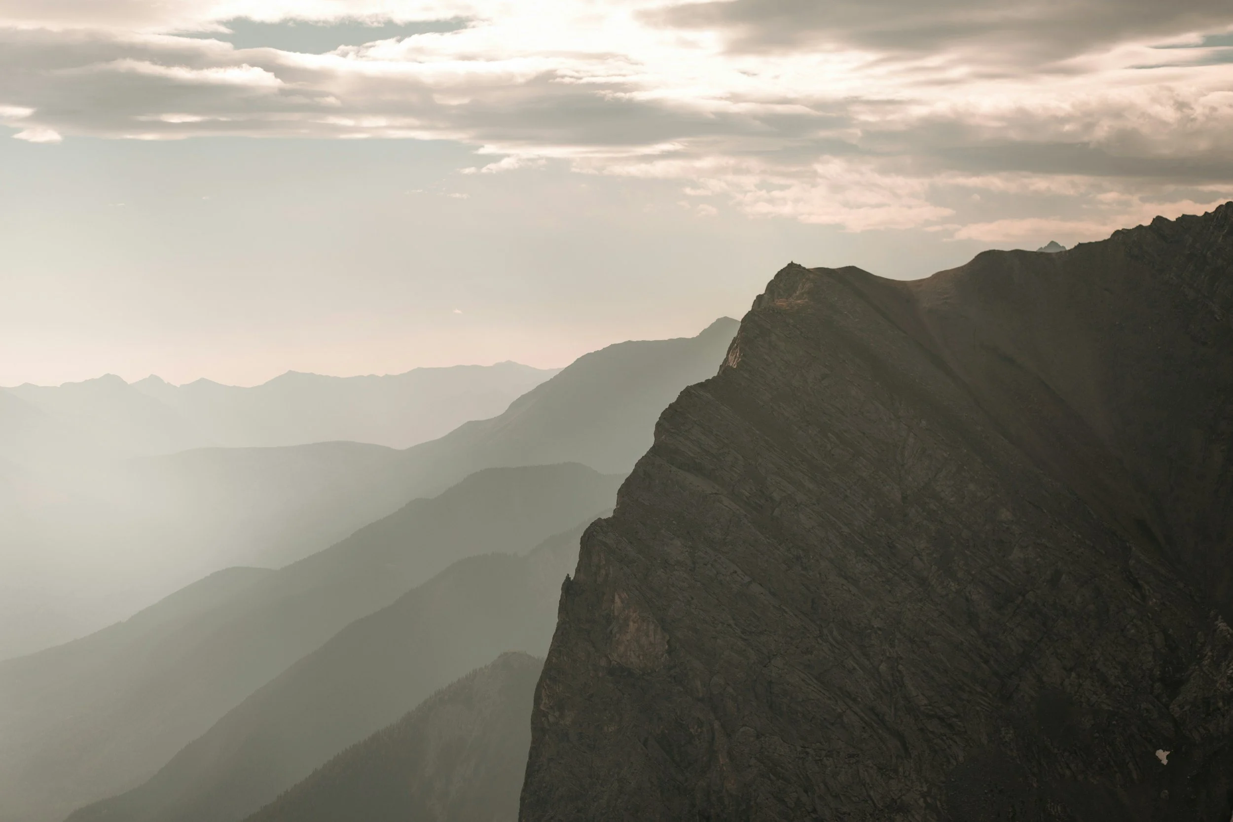 Scenic mountain landscape with rugged cliffs and layered mountain ranges under a cloudy sky.