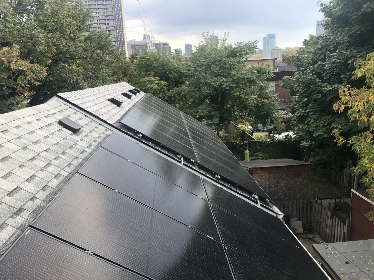 A roof with solar panels installed, surrounded by trees and a city skyline in the background.