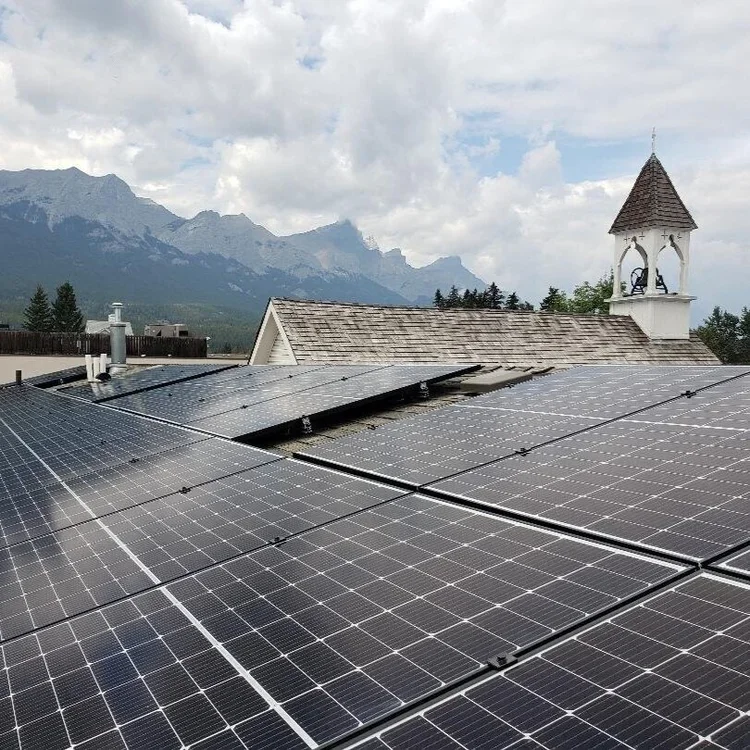 Solar panels on a rooftop with mountains and a cloudy sky in the background.