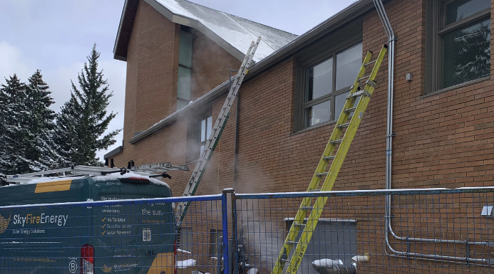 A building with ladders and a work van nearby, with steam or smoke coming from the roof or upper part of the building.