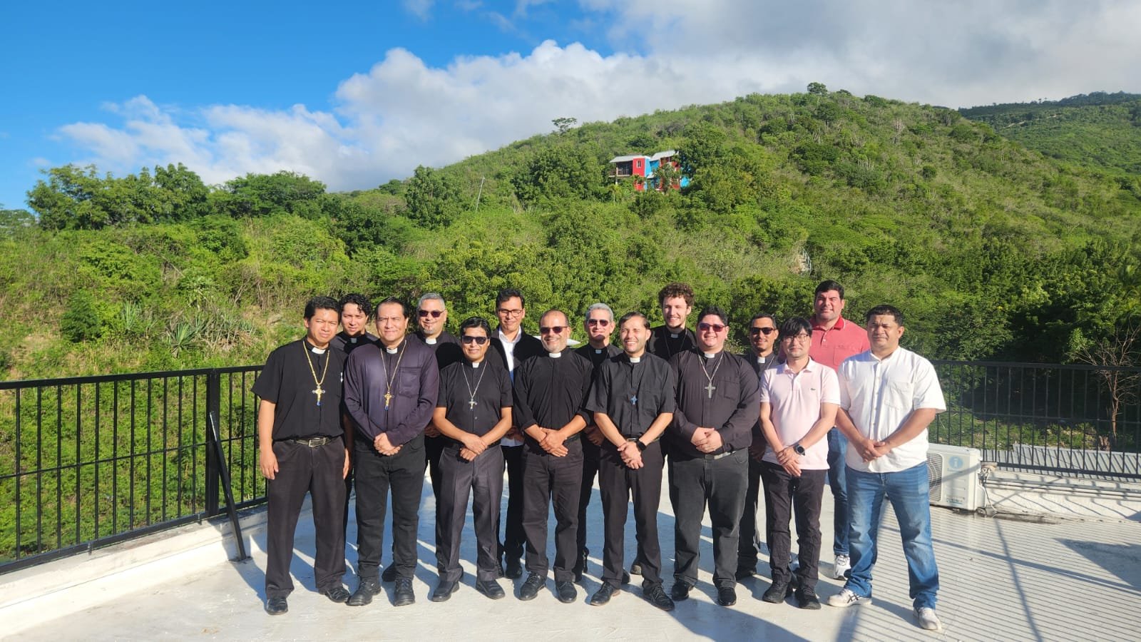 Grupo de personas con vestimentas religiosas posando en la azotea con montañas verdes y cielo azul de fondo.