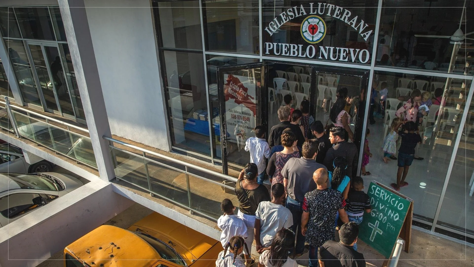 Museo iglesia luterana en pueblo nuevo con gente haciendo fila en la entrada, carteles con información y coches estacionados.