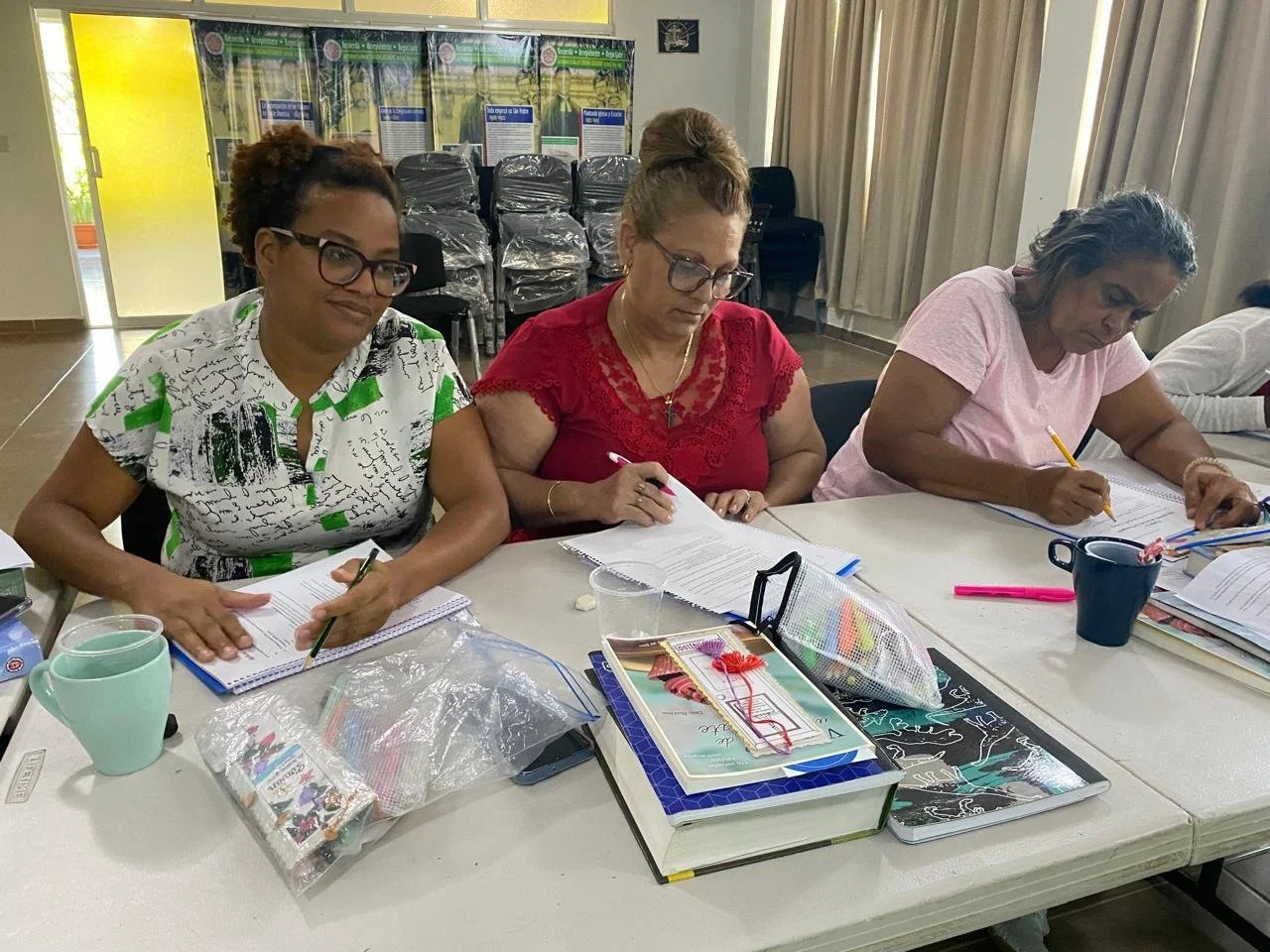 Mujeres sentadas en una mesa tomando notas en un aula de clases.