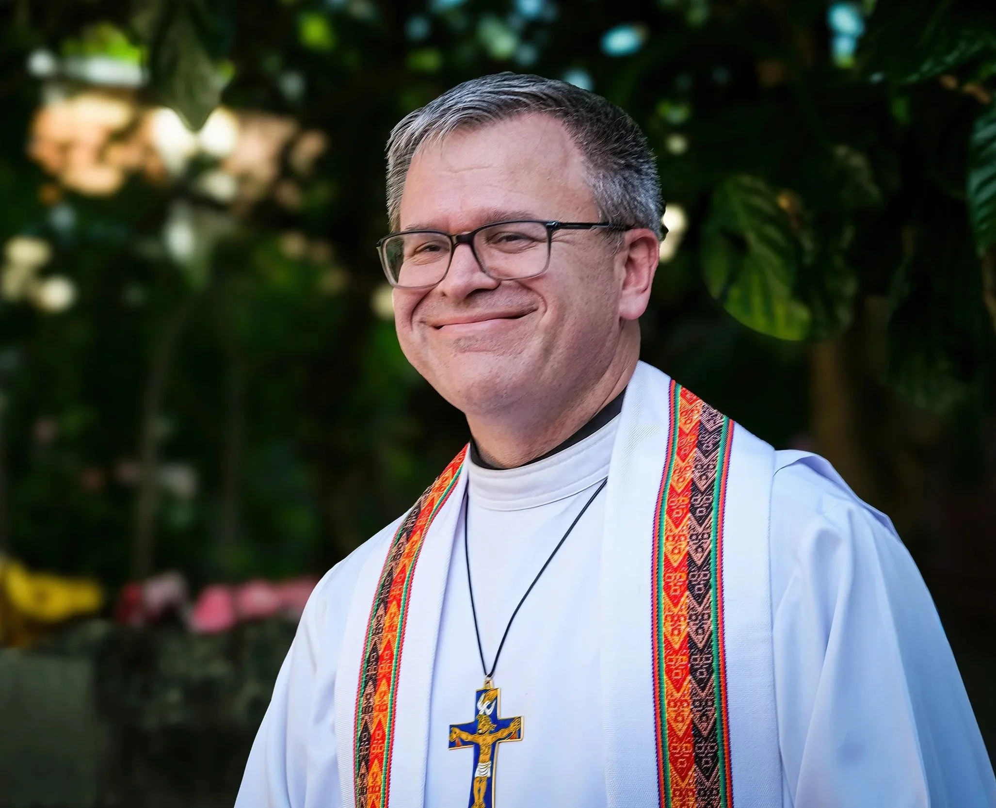 Un pastor luterano, vestido con ropa tradicional y collar con cruz, en un entorno natural con árboles en el fondo.