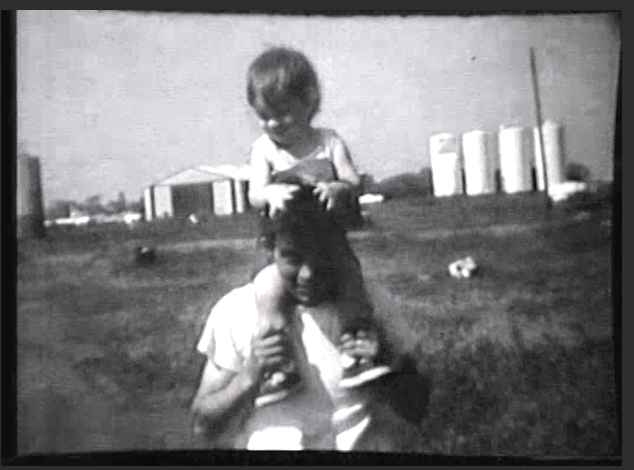 A black-and-white photo of Elizabeth Meister when she was three, perched  shoulders of her dad, Rodney Meister, outdoors in the train yard where he worked in Dwight, Illinois, 1974.