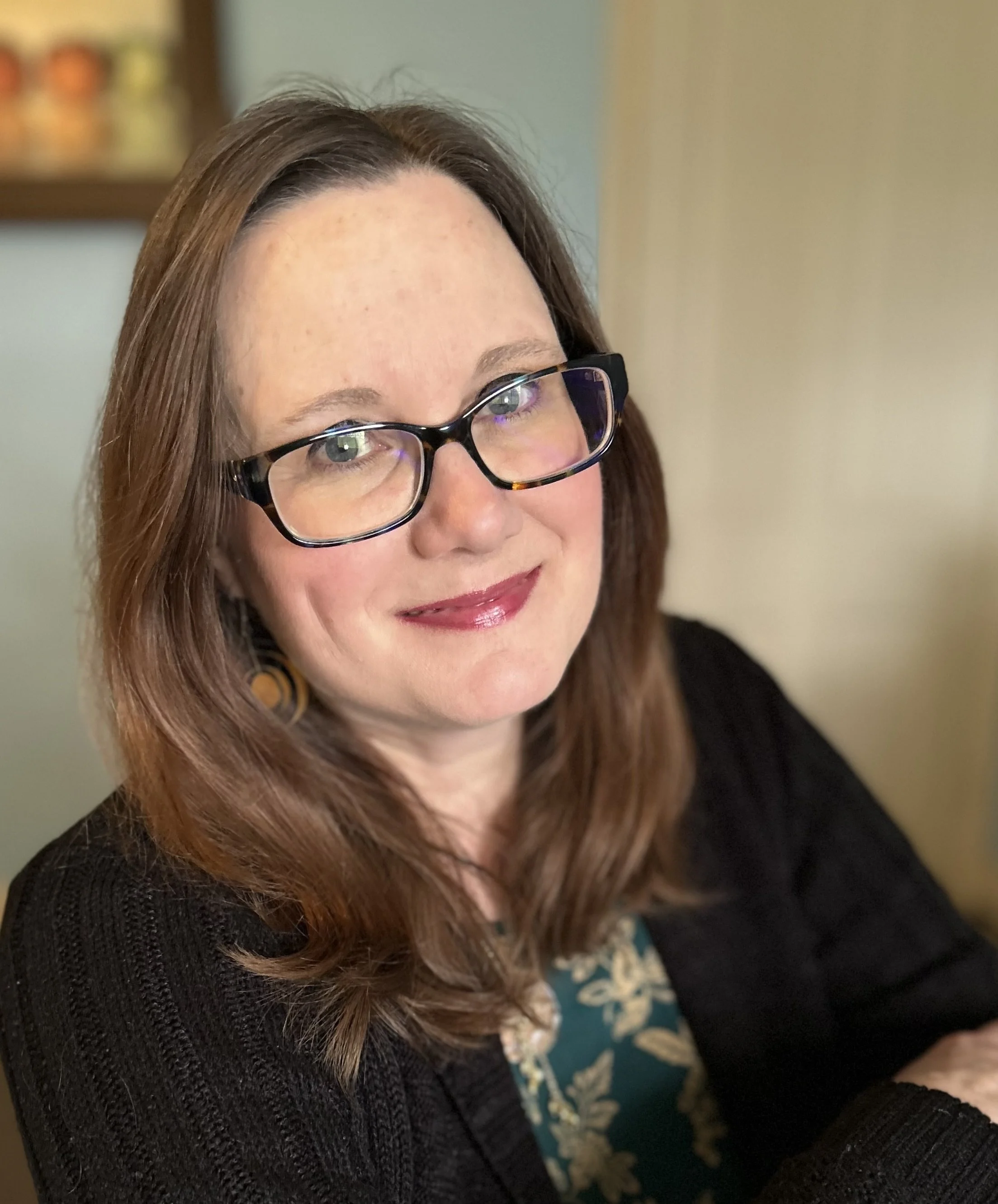 Head and shoulders photograph of Lisa Nanni, with medium length brown hair and glasses, smiling and wearing a black sweater and earrings.