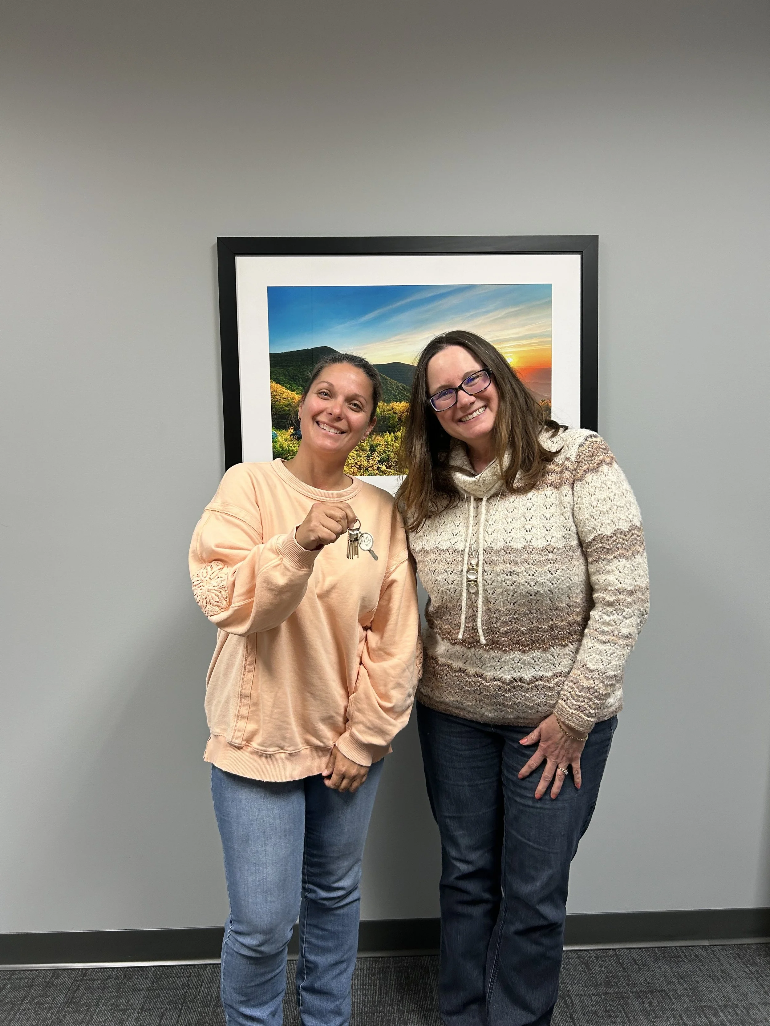 Lisa Nanni and client Jennyfer, moments after closing. They're in a conference room in an office setting. They're standing side by side, beaming smiles. Jennyfer is proudly holding her new house keys.