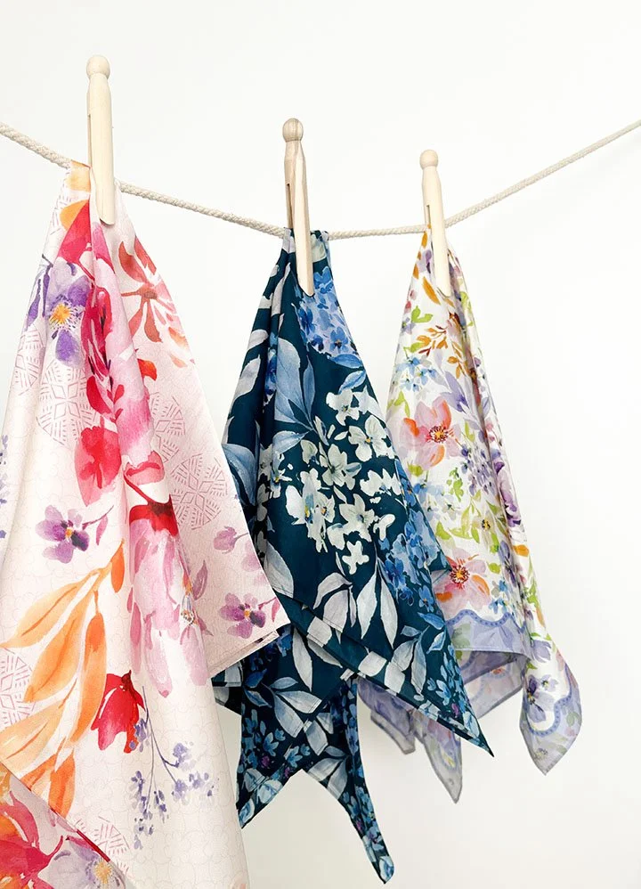 Three colorful floral scarves hanging on a clothesline secured with wooden clothespins.