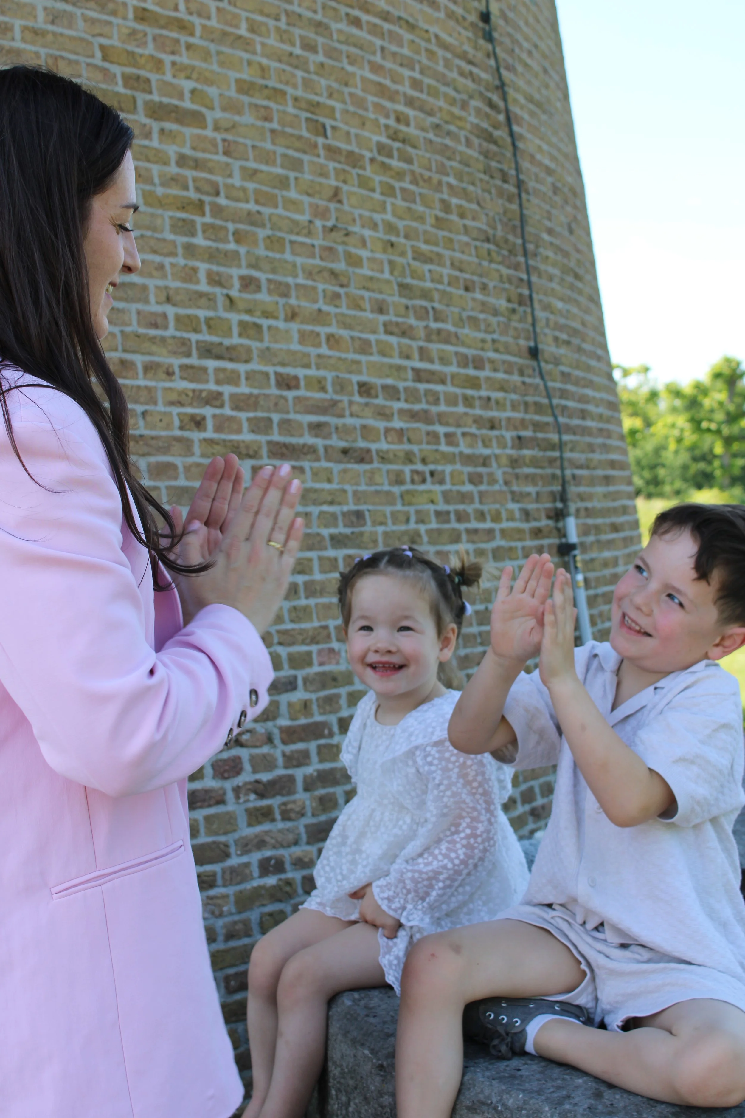 A woman and three children smiling and giving high fives outside near a brick wall.