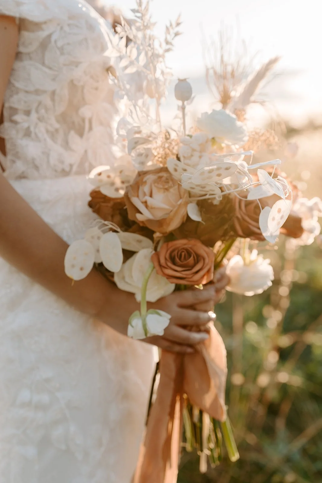 A bride holding a bouquet of roses, white flowers, and other greenery during sunset.