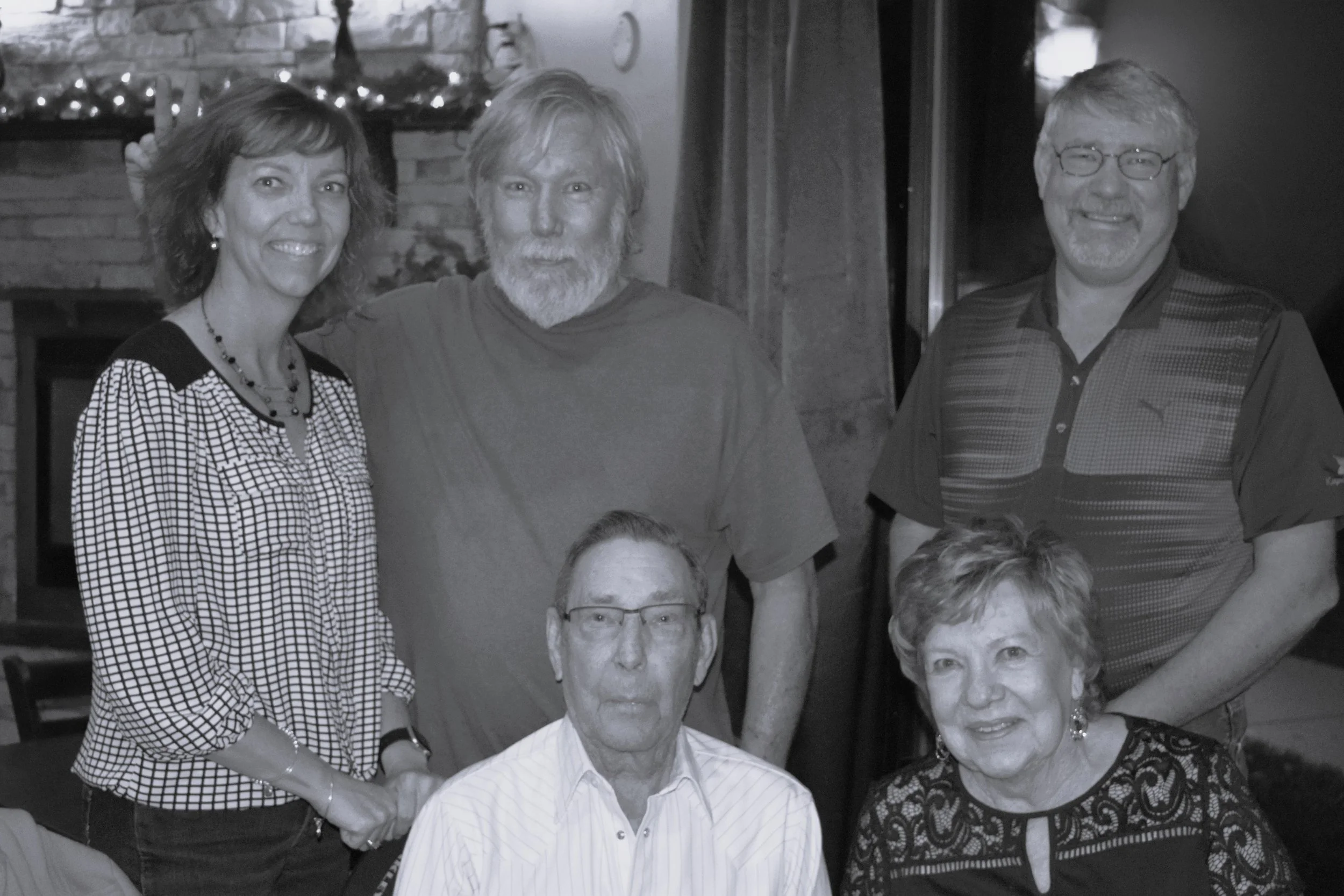 Group of six smiling people in a restaurant or bar, some sitting and some standing, with Christmas decorations in the background.