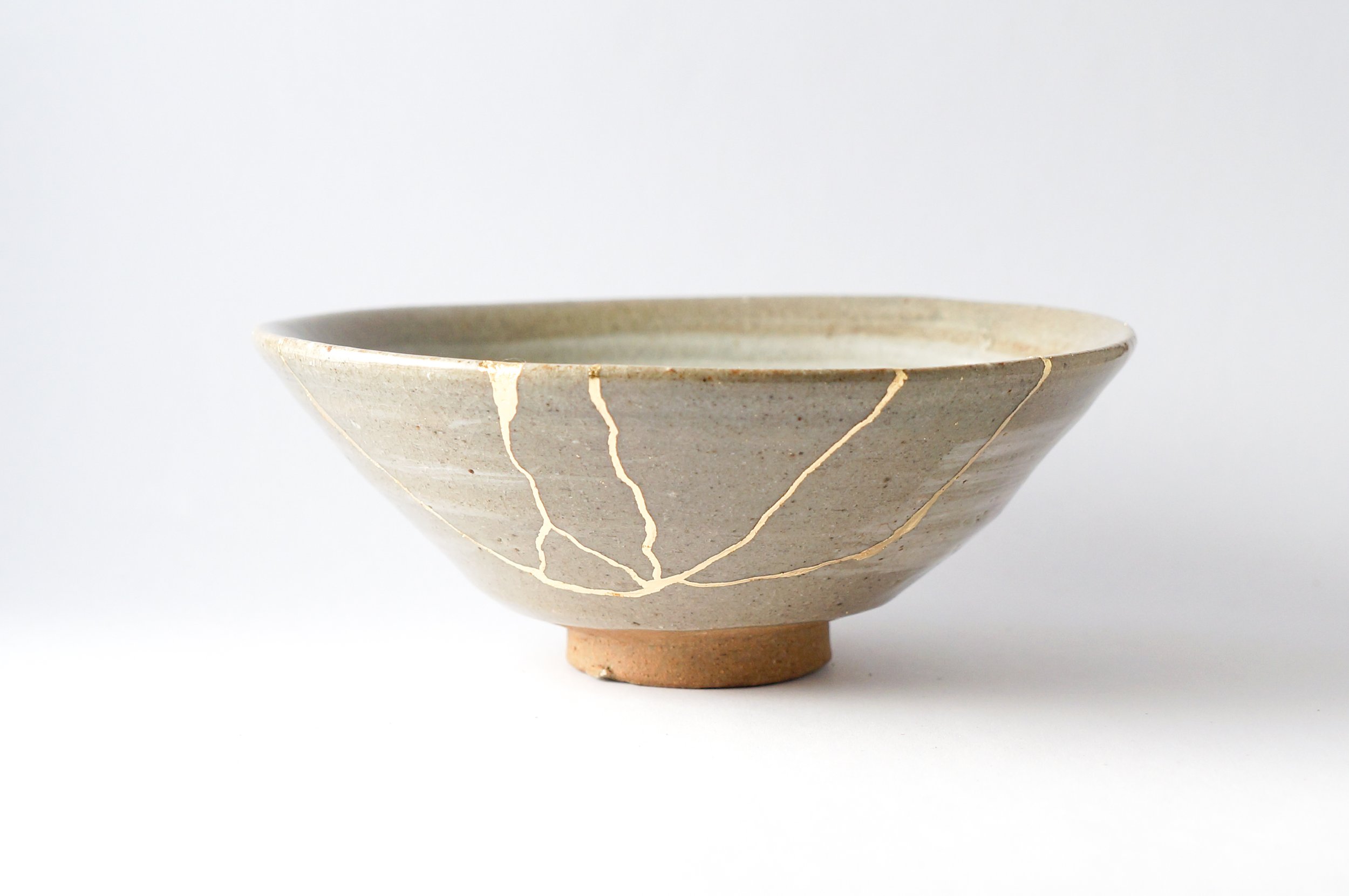 A ceramic bowl with a beige, speckled glaze, decorated with white crackle patterns, on a small pedestal base, against a plain white background.