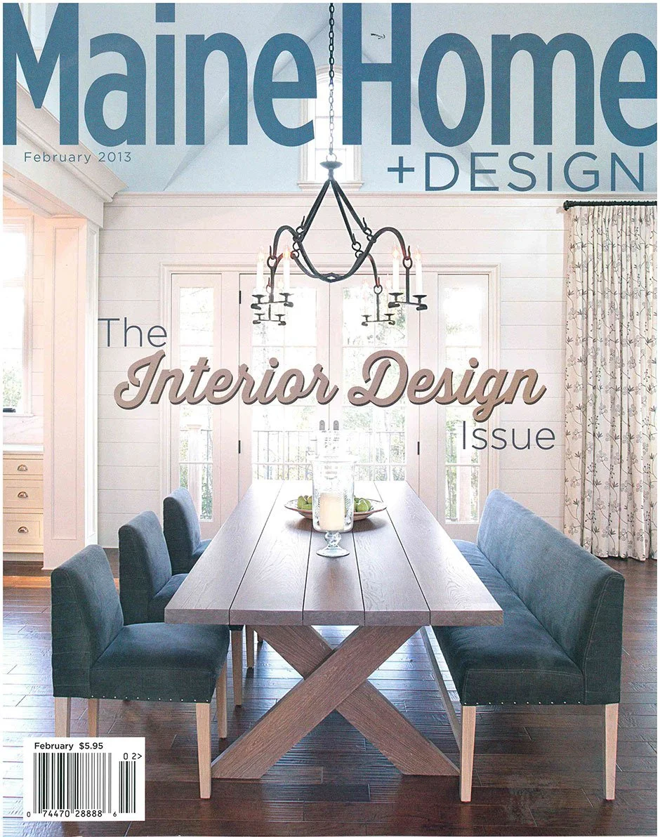 The cover of Mainer Home + Design magazine, February 2013 issue, featuring an interior view of a dining room with a wooden table, black upholstered chairs, a chandelier, and a background of white walls with windows and curtains.