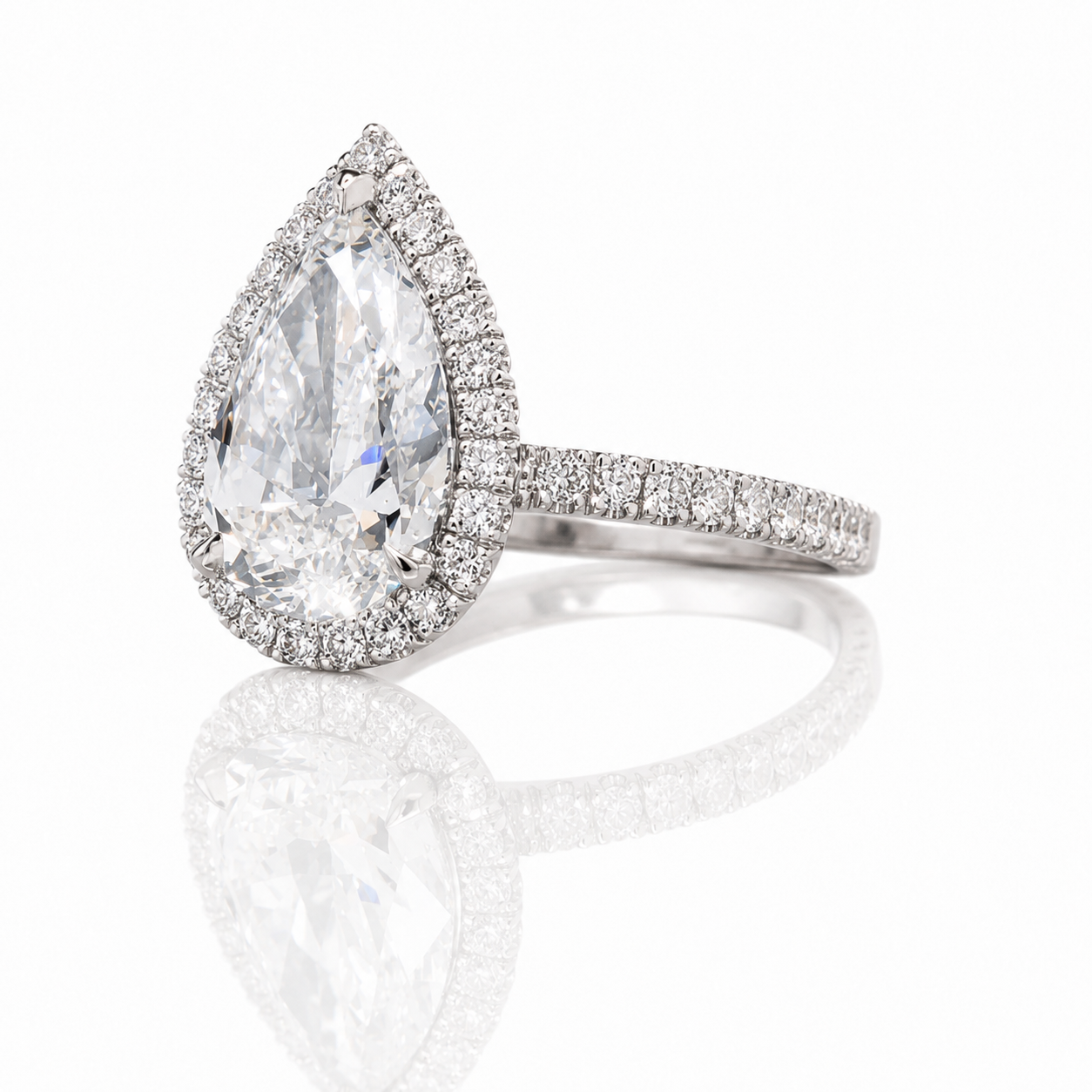A jewelry ring with a large teardrop-shaped diamond surrounded by smaller diamonds on a silver band, reflected on a shiny surface.
