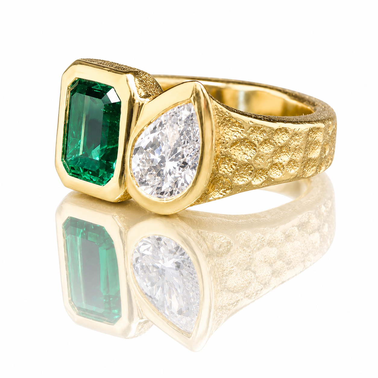 Gold ring with a large green emerald and a tear-shaped diamond on a reflective white surface.