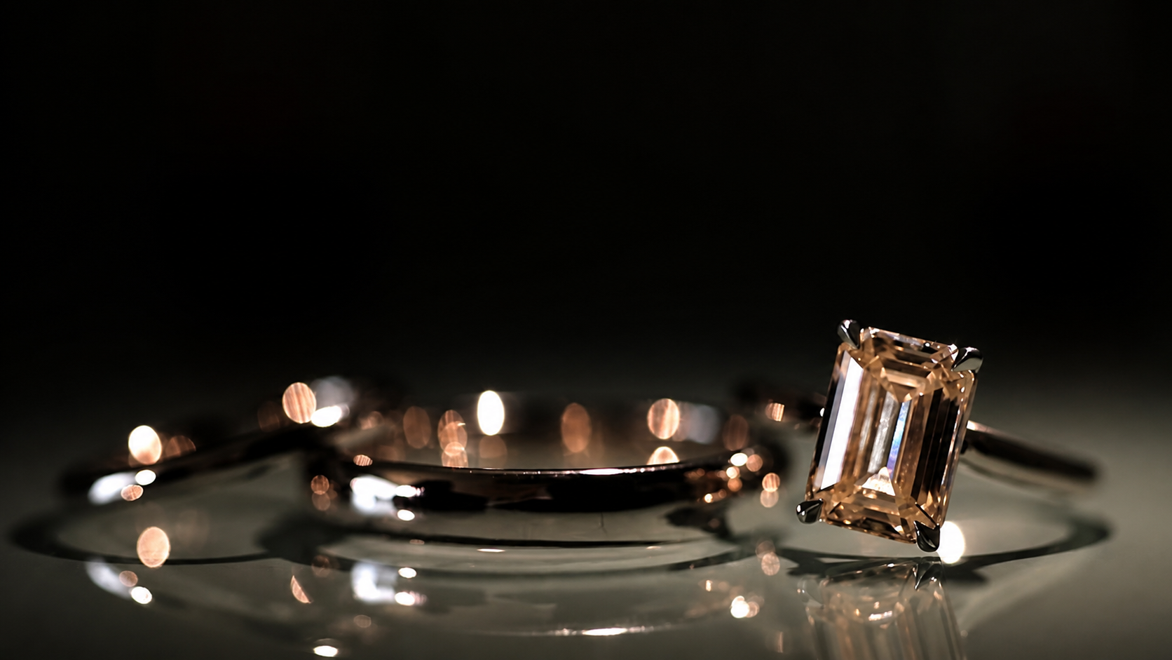 Close-up of a diamond ring with a rectangular cut stone and a diamond bracelet on a reflective surface under soft lighting.