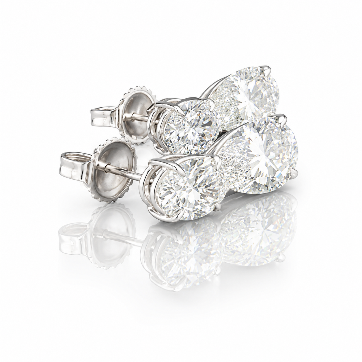Pair of silver stud earrings with large round-cut diamonds on a white reflective surface.