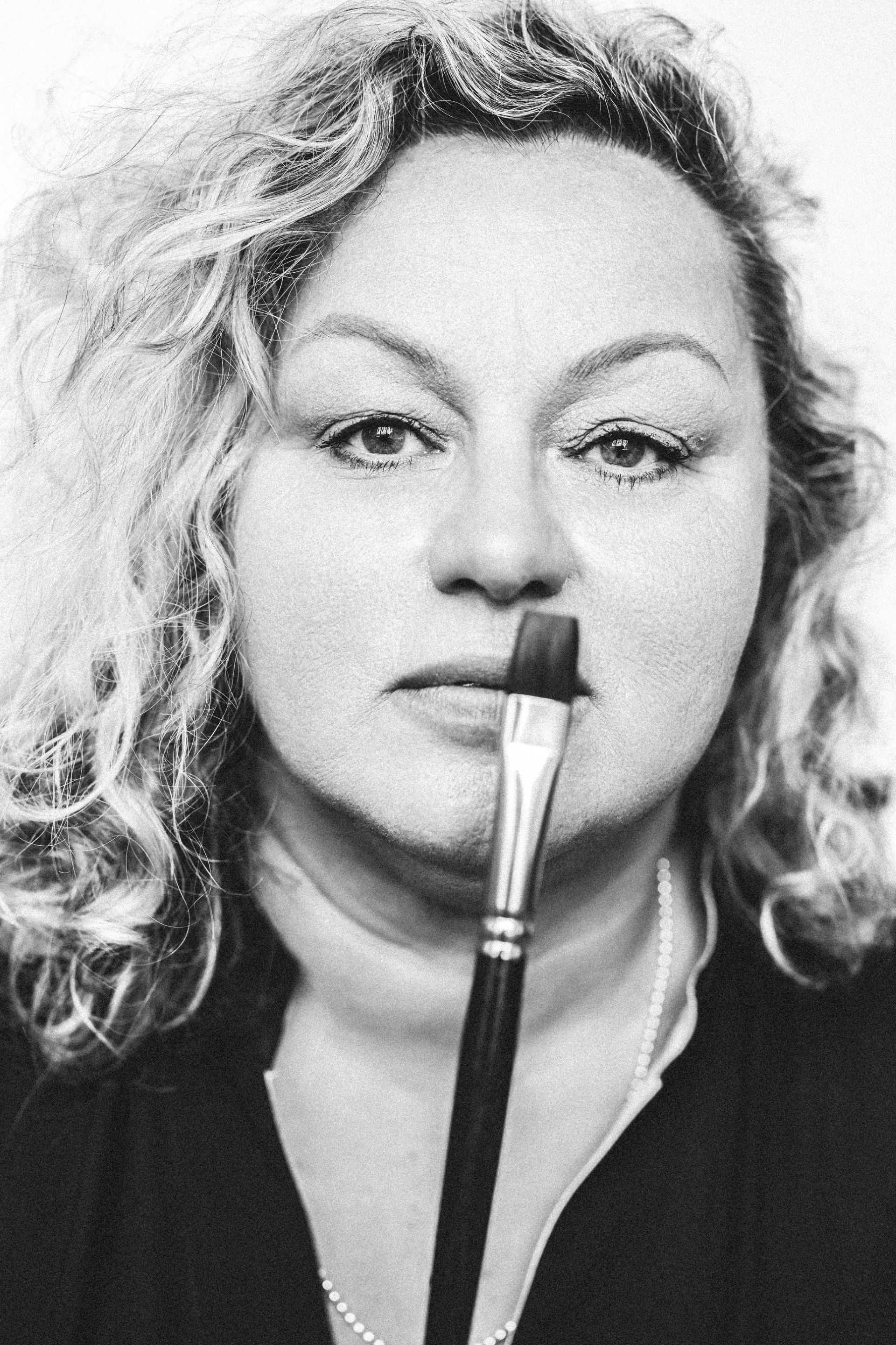 A woman with curly hair applying lipstick in front of a mirror, with her face partially visible.