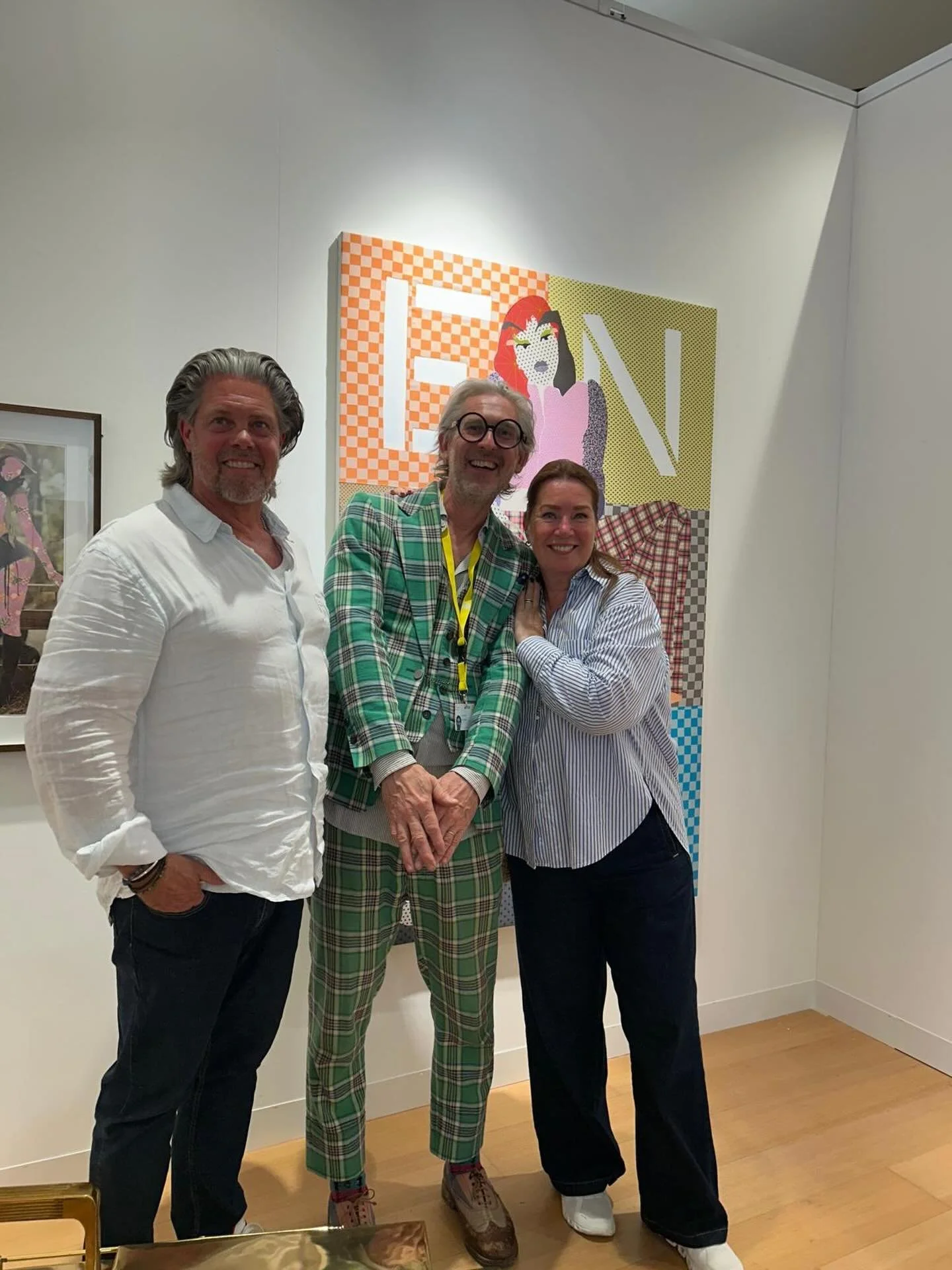 Three people standing together in front of colorful artwork, smiling for the camera.