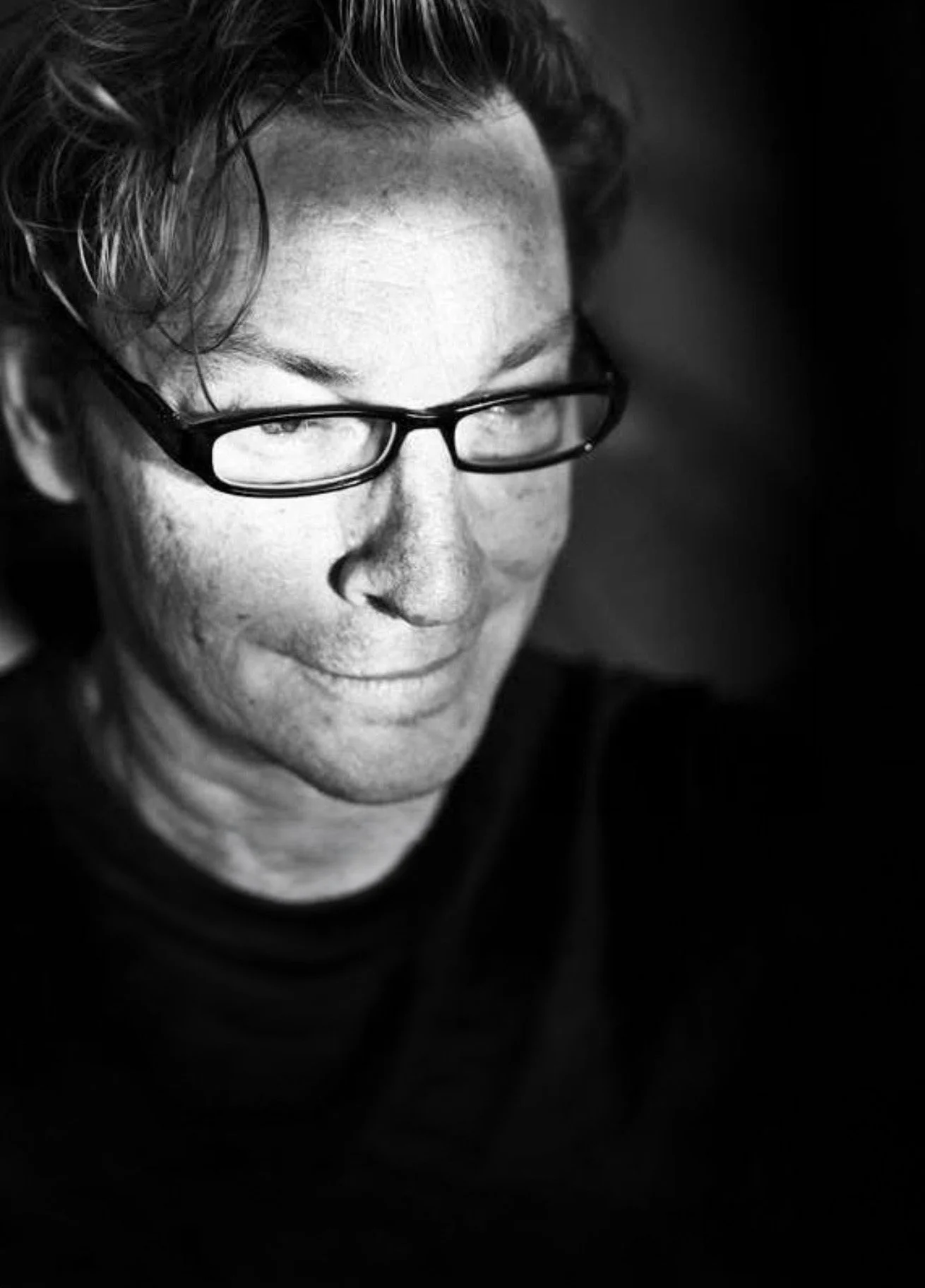 A black and white close-up portrait of a man with glasses, short wavy hair, and a slight smile.